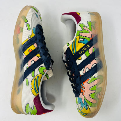 The Adidas Gazelle Indoor Sean Wotherspoon sneaker, with colorful abstract uppers in yellow, red, pink, and green, dark blue stripes, red laces, and translucent soles, rests on a blue box showing size and product details.