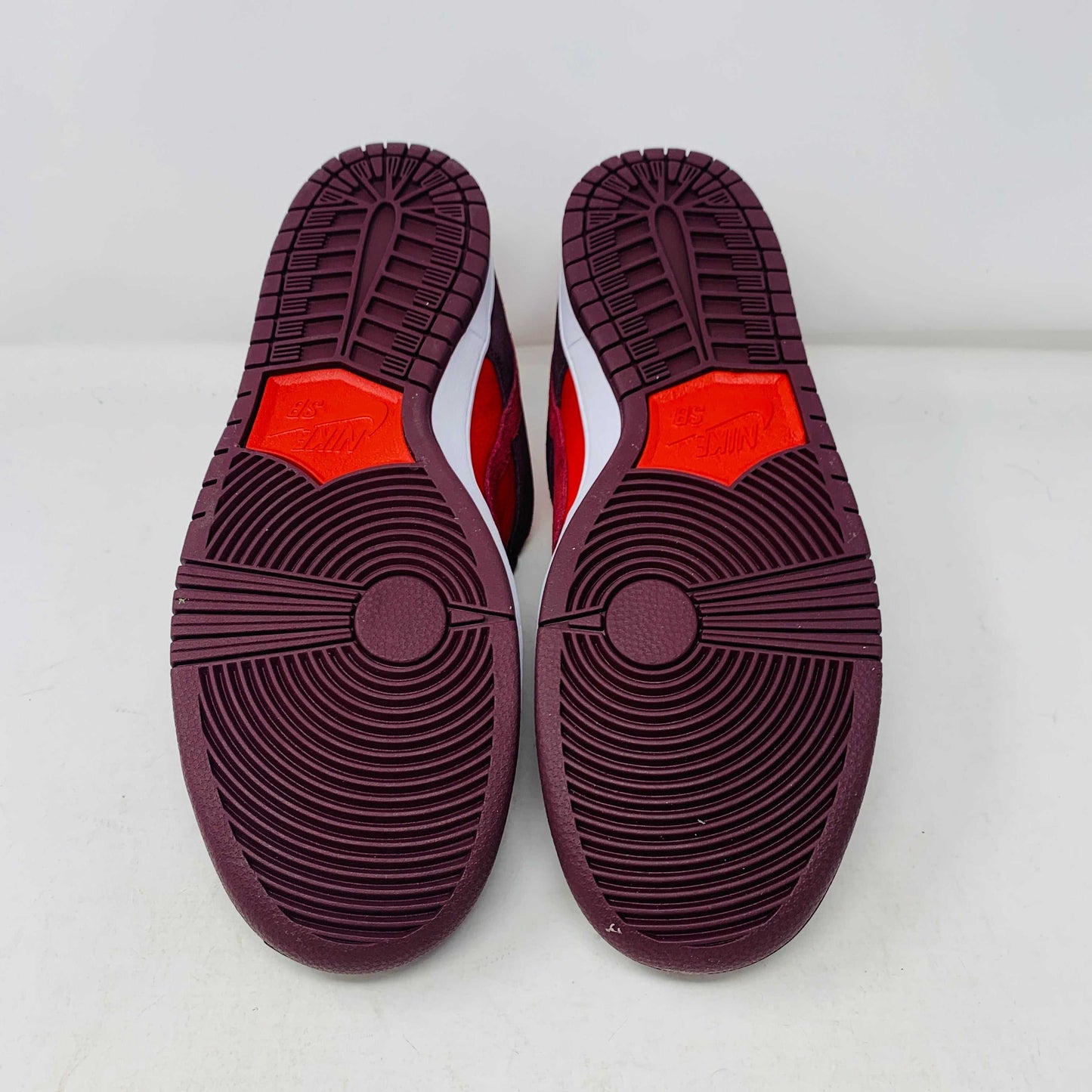 A 100% authentic, brand new Nike SB Dunk Low Cherry sneaker in red and dark brown sits on a branded purple Nike SB shoebox. It features a red swoosh, toe box, dark brown overlays, extra laces, white midsole, and dark brown outsole.