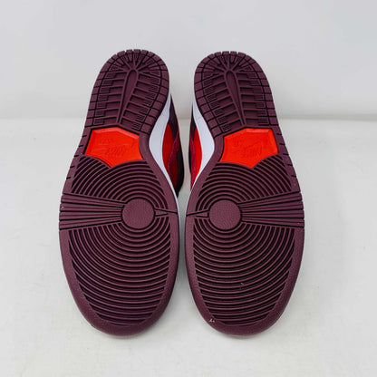 A 100% authentic, brand new Nike SB Dunk Low Cherry sneaker in red and dark brown sits on a branded purple Nike SB shoebox. It features a red swoosh, toe box, dark brown overlays, extra laces, white midsole, and dark brown outsole.