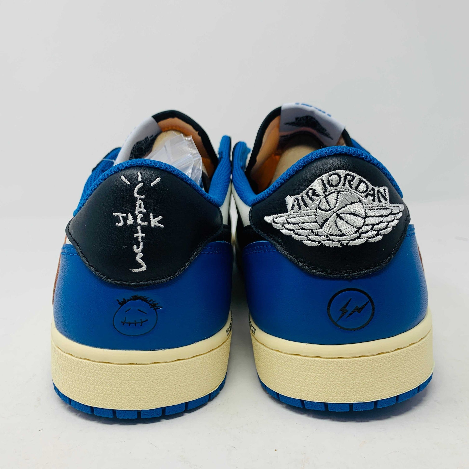 The Jordan 1 Low Travis Scott x Fragment sneakers feature a black and white leather upper with blue accents, a unique beige backward swoosh, and come in a branded Nike box with graphics. These brand-new shoes include an extra set of laces for added versatility.
