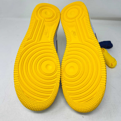 The Nike Air Force 1 Low Retro QS Kobe Bryant Lakers Home sneakers showcase their bright yellow soles with intricate tread patterns, featuring circular grooves and textured edges, positioned soles up.