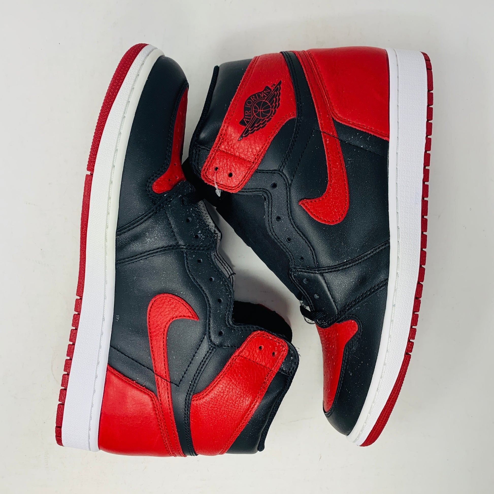The Jordan 1 High Bred 2016 sneakers, by Jordan, are brand-new black and red high-tops with a white sole. Viewed from above, they showcase an unlaced look with a perforated design on the toe area.