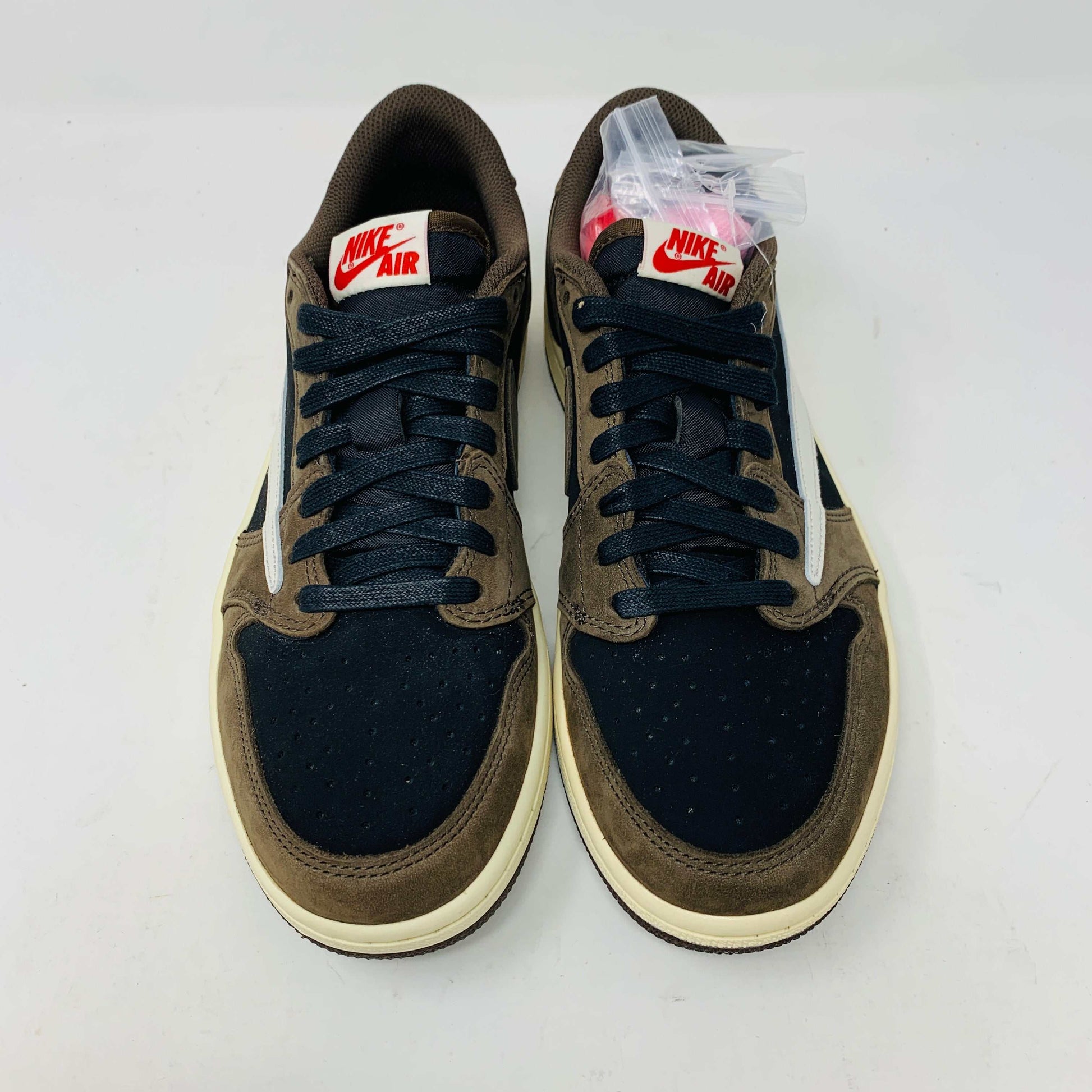 A pair of BRAND NEW Jordan 1 Low OG Travis Scott Mocha sneakers in black and brown, featuring a white swoosh, displayed on a brown shoe box with a red logo. 100% Authentic with EXTRA LACES partially visible inside.