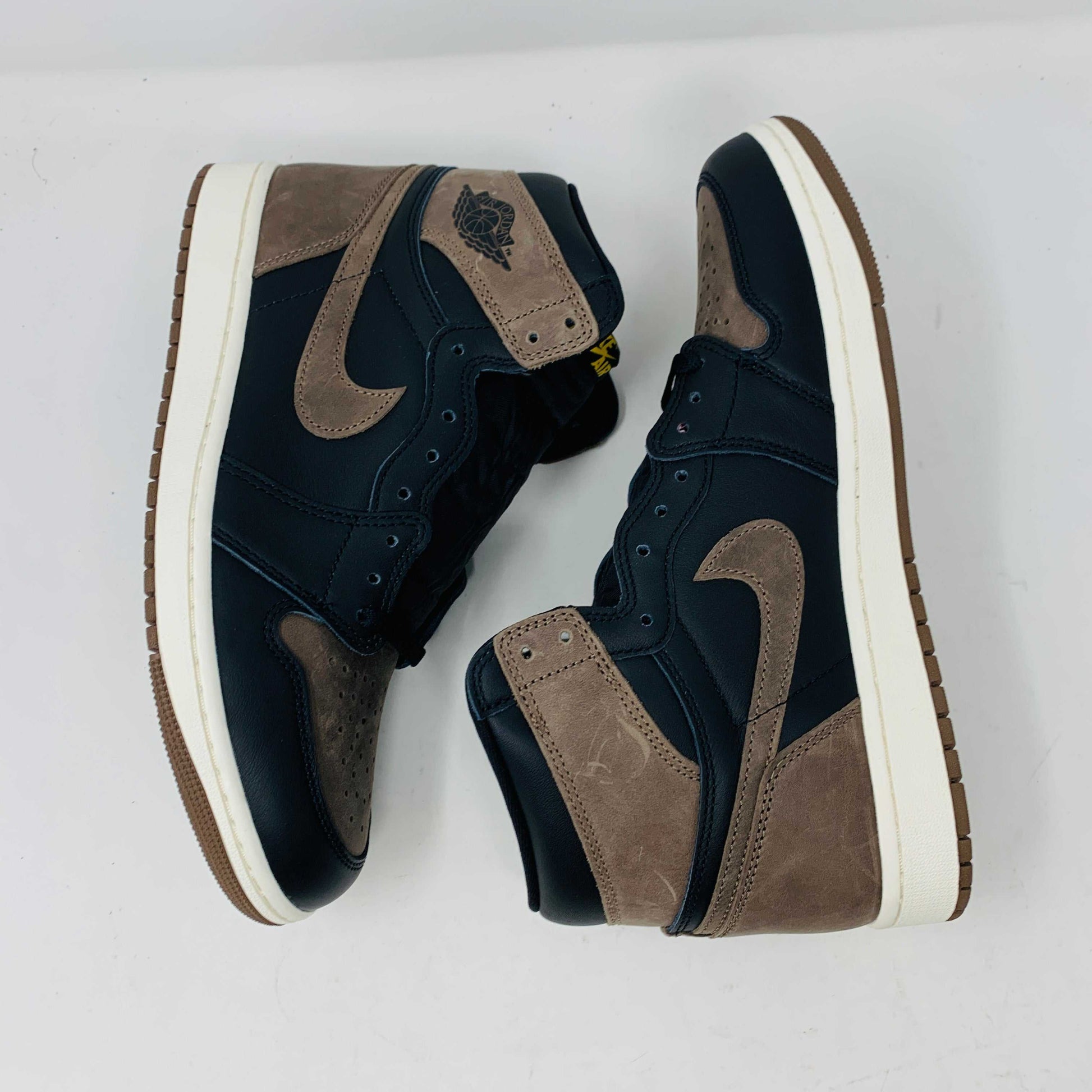 The Jordan 1 Retro High OG Palomino, a new black and brown sneaker from the Jordan brand, is displayed atop a pristine black and yellow Nike shoebox. The 2023 high-top design features the signature swoosh and Air Jordan logo, emphasizing its fresh-off-the-shelf allure.