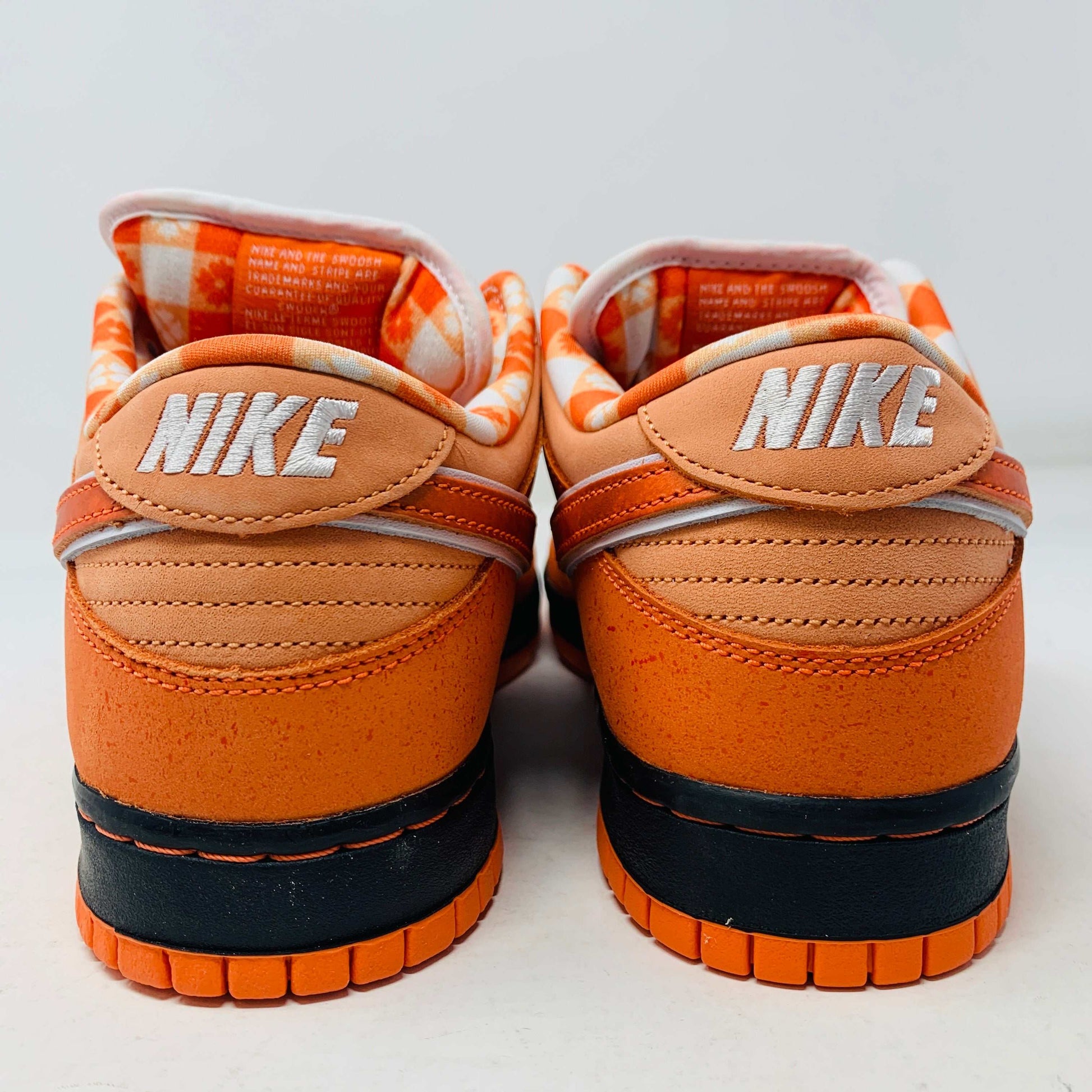 The authentic Nike SB Dunk Low Orange Lobster Concepts sneaker sits on a green and yellow Nike SB box. It features a white sole with black trim, an orange swoosh, and extra laces neatly positioned in front of the box.