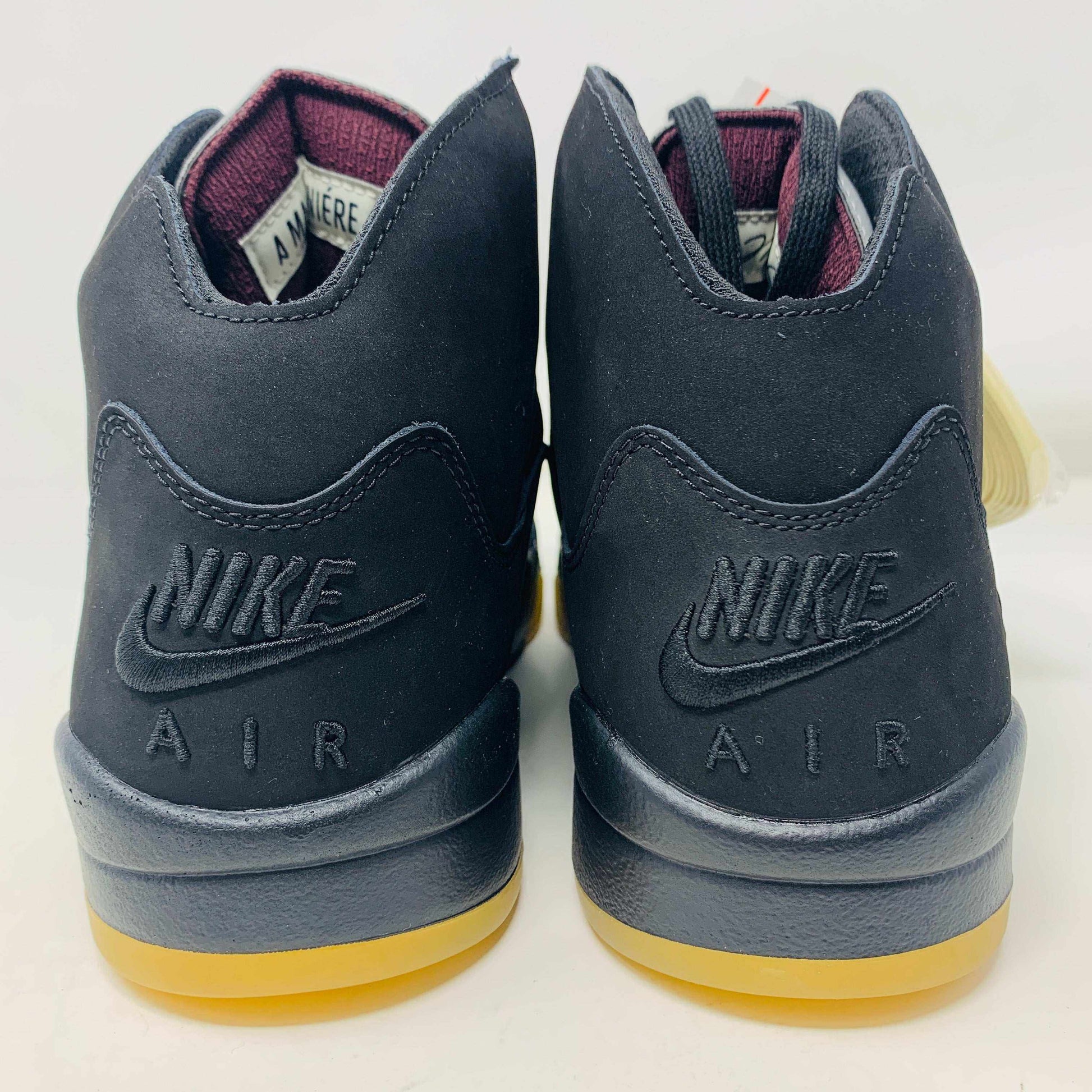 A pair of Jordan 5 Retro A Ma Maniére Dusk sneakers by Jordan, featuring a black exterior with NIKE AIR embossed on the back, a maroon inner lining, and a gum-colored sole.