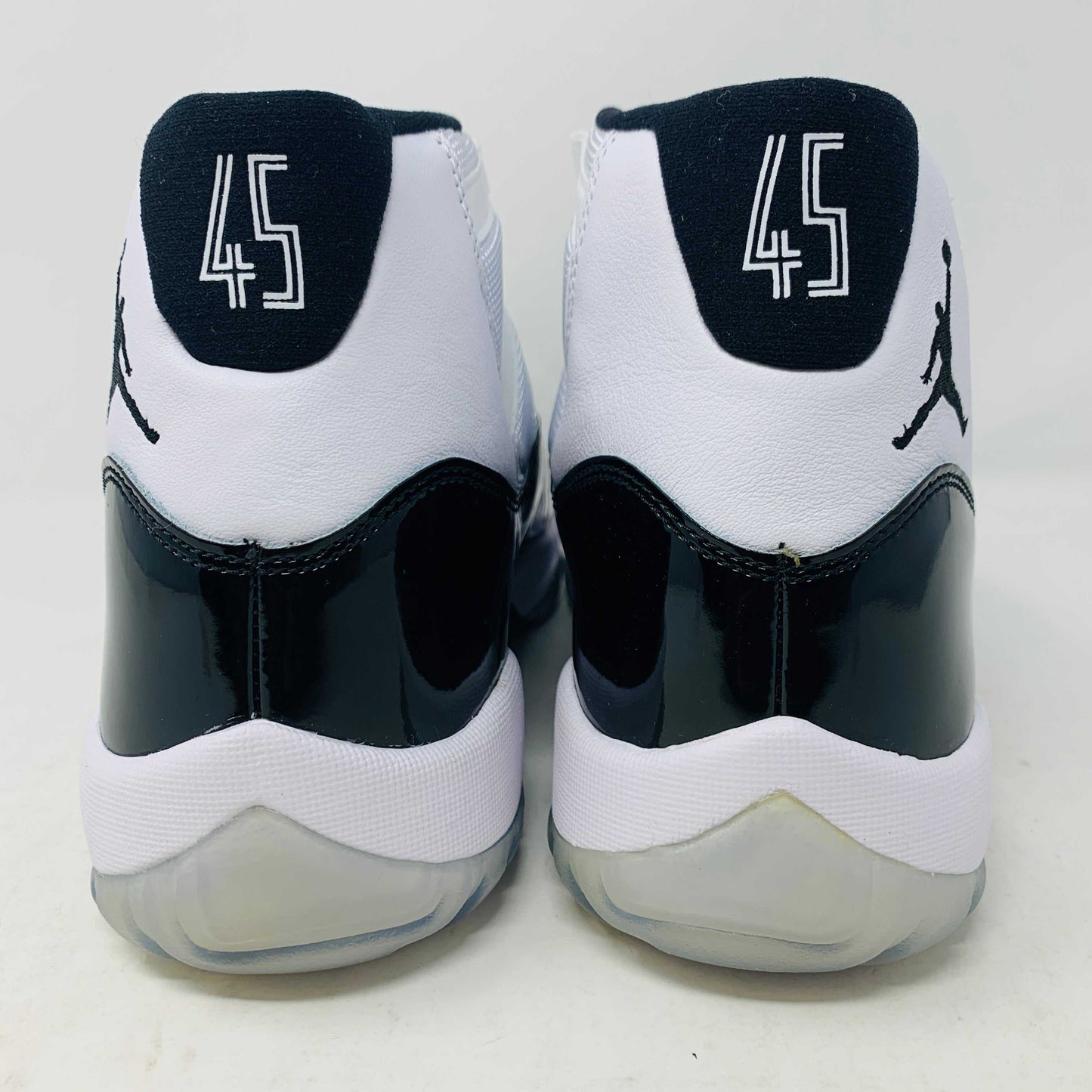 A BRAND NEW black and white Jordan 11 Concord 2018 sneaker sits on its shoebox, showcasing a glossy black patent leather finish and white mesh upper with the iconic Jumpman logo. The shoebox, bearing a white Nike Air logo, ensures these shoes are 100% authentic.