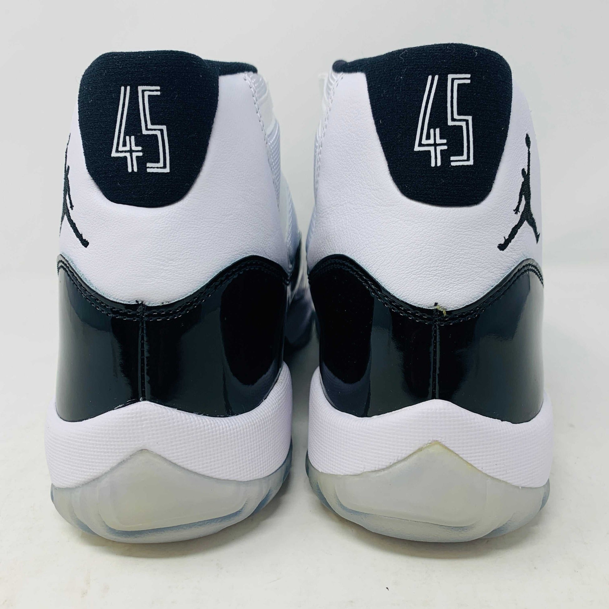 A BRAND NEW black and white Jordan 11 Concord 2018 sneaker sits on its shoebox, showcasing a glossy black patent leather finish and white mesh upper with the iconic Jumpman logo. The shoebox, bearing a white Nike Air logo, ensures these shoes are 100% authentic.