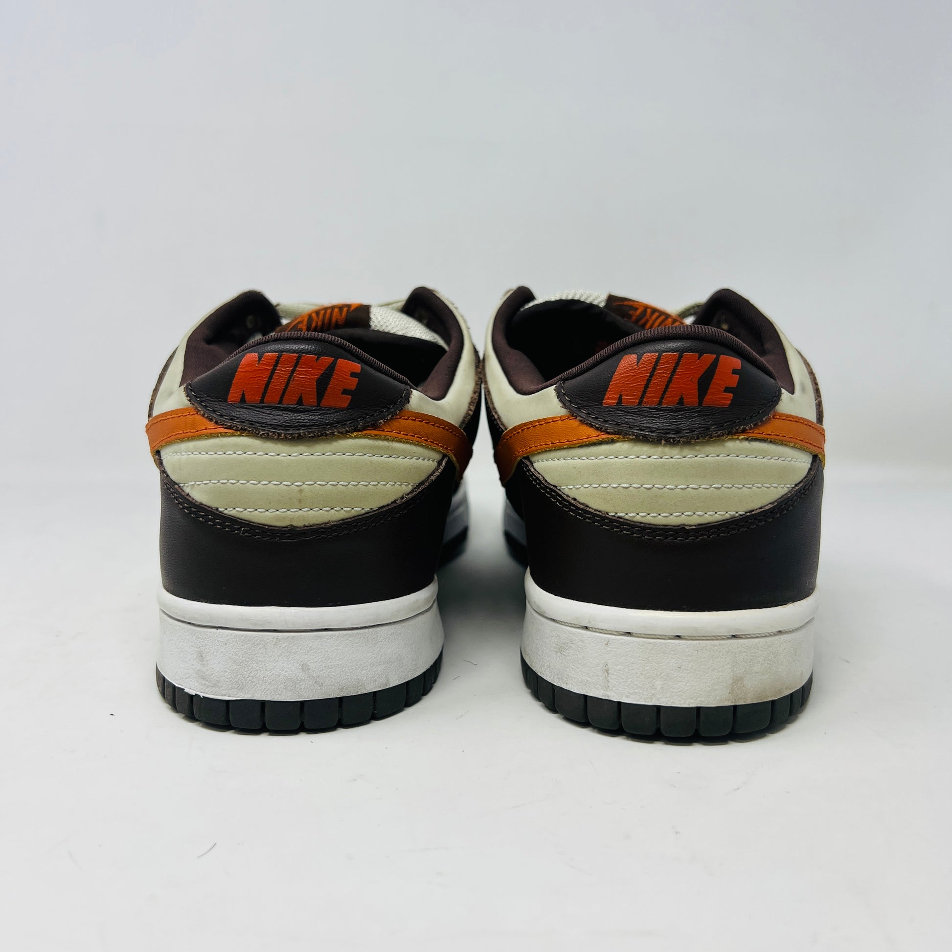 The Nike Dunk Low Pro B Light Stone Mesa Orange sneaker from 2002 is shown side-on, featuring sleek uppers in dark brown and cream with an orange swoosh. It rests elegantly on a white midsole with a black outsole against a plain background.