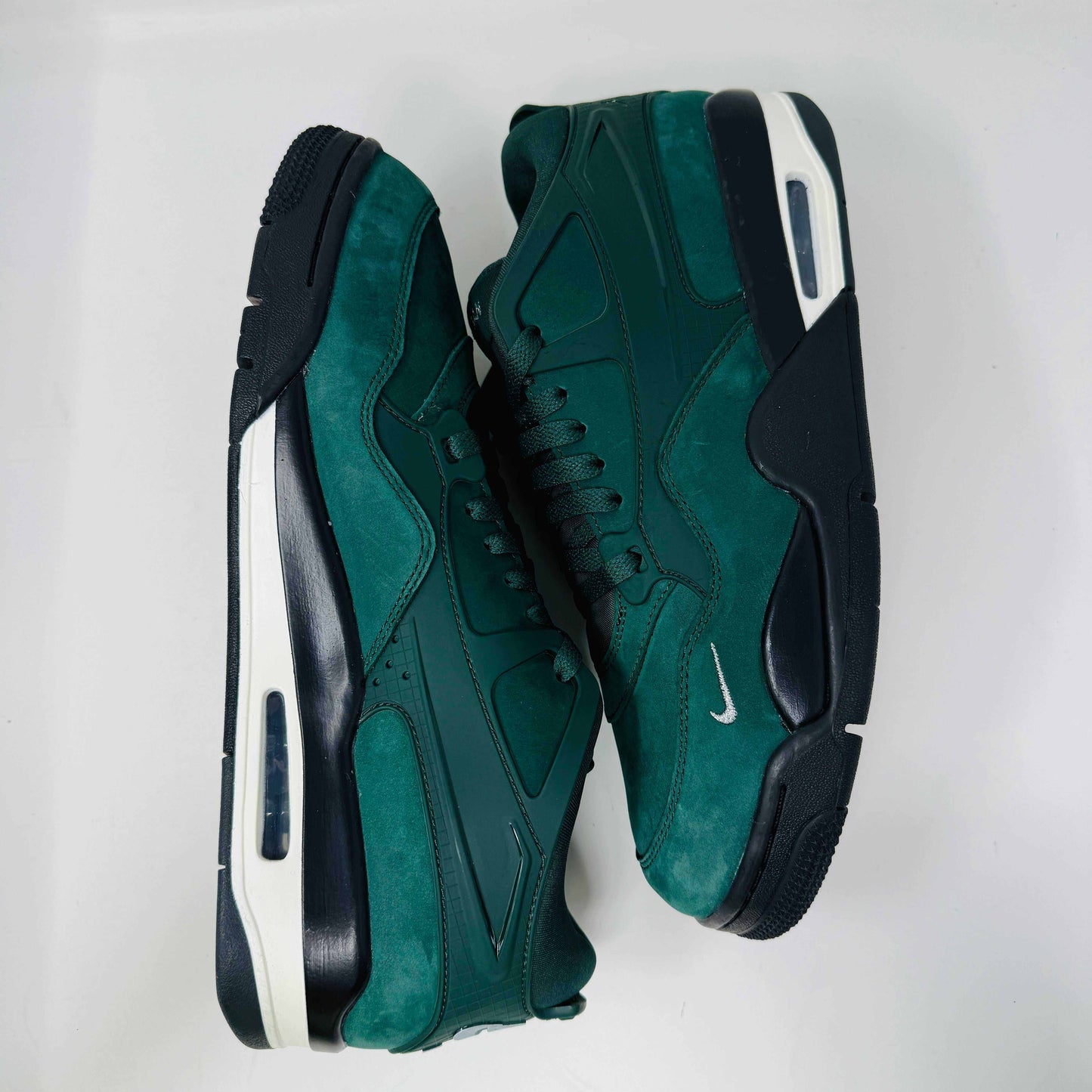 The Jordan 4 RM SP Nigel Sylvester Grandmas Driveway sneakers feature a dark green color with Air by Jordan on the tongue in white, accented with white laces and a low-top design, all set against a plain white background.
