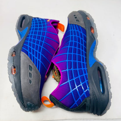 Displayed on an orange Nike shoe box is the colorful Nike Air Max Sunder SP Kids of Immigrants Sun Down sneaker, featuring a grid pattern with shades of purple, blue, and gray, complemented by orange accents and a swoosh logo. The shoe box shows a k-i logo inside a circle.