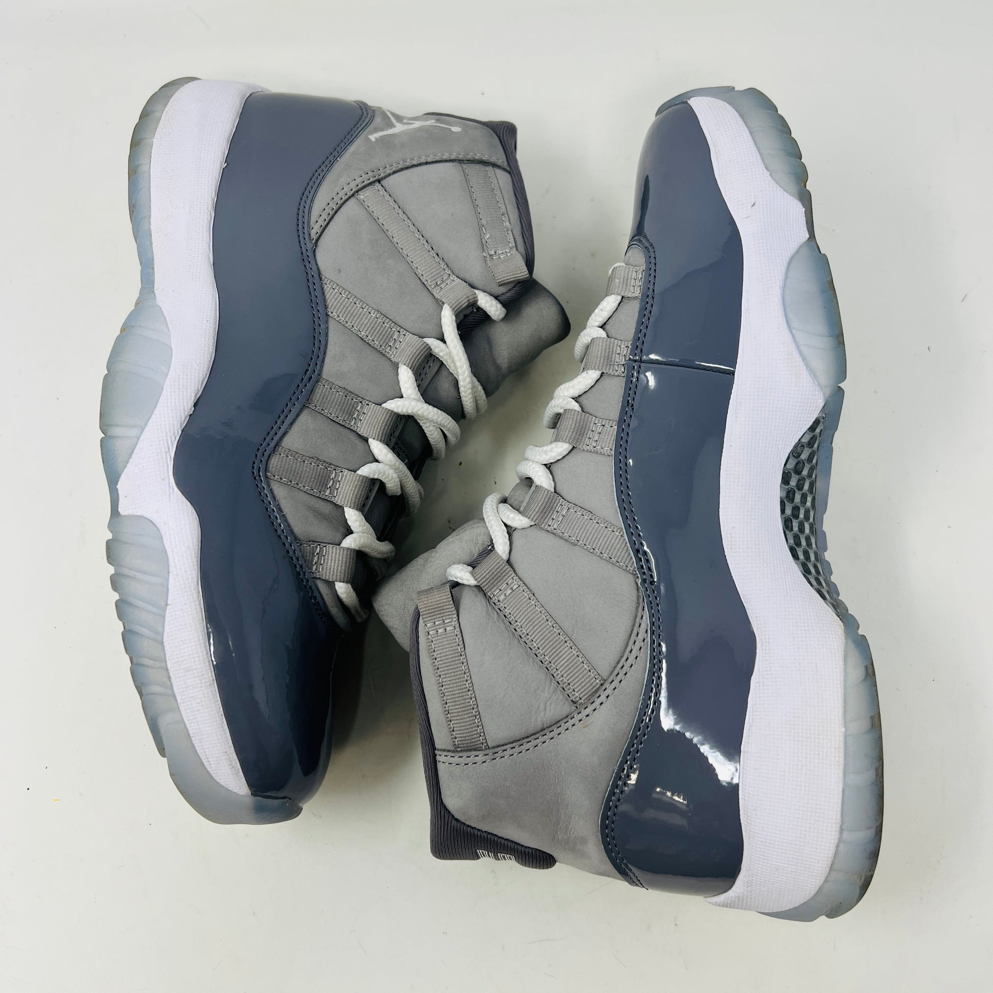 The Jordan 11 Retro Cool Grey (2021) sneaker, featuring clean gray and white uppers with glossy patent leather accents and white laces, is displayed on a gray Nike Air shoebox. The shoe is authentic in size 9.5, with the box in good condition.