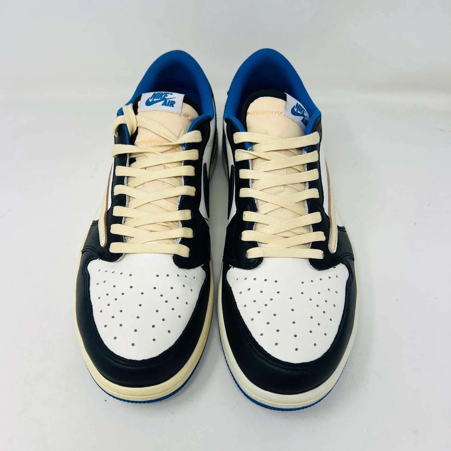 The Jordan 1 Retro Low OG SP Fragment x Travis Scott sneaker, with a blue, black, and white color scheme, sits on a Nike box. Two extra shoelace pairs in black and pink are included in clear bags to keep your look fresh with authentic VNDS style.