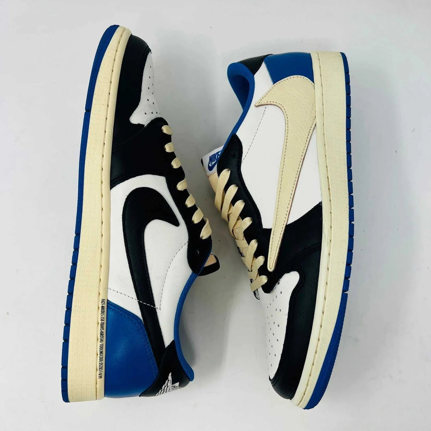 The Jordan 1 Retro Low OG SP Fragment x Travis Scott sneaker, with a blue, black, and white color scheme, sits on a Nike box. Two extra shoelace pairs in black and pink are included in clear bags to keep your look fresh with authentic VNDS style.