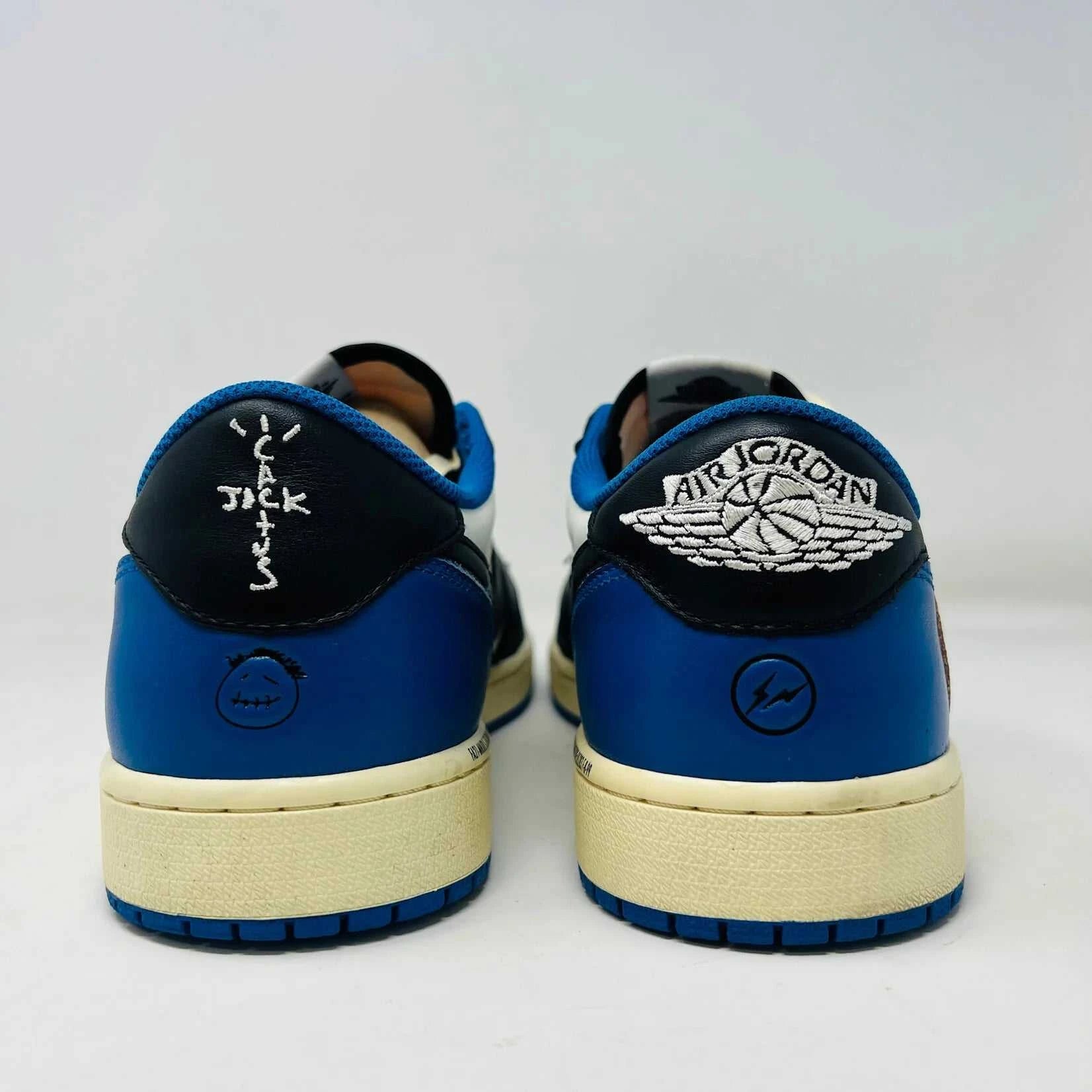 The Jordan 1 Retro Low OG SP Fragment x Travis Scott sneaker, with a blue, black, and white color scheme, sits on a Nike box. Two extra shoelace pairs in black and pink are included in clear bags to keep your look fresh with authentic VNDS style.