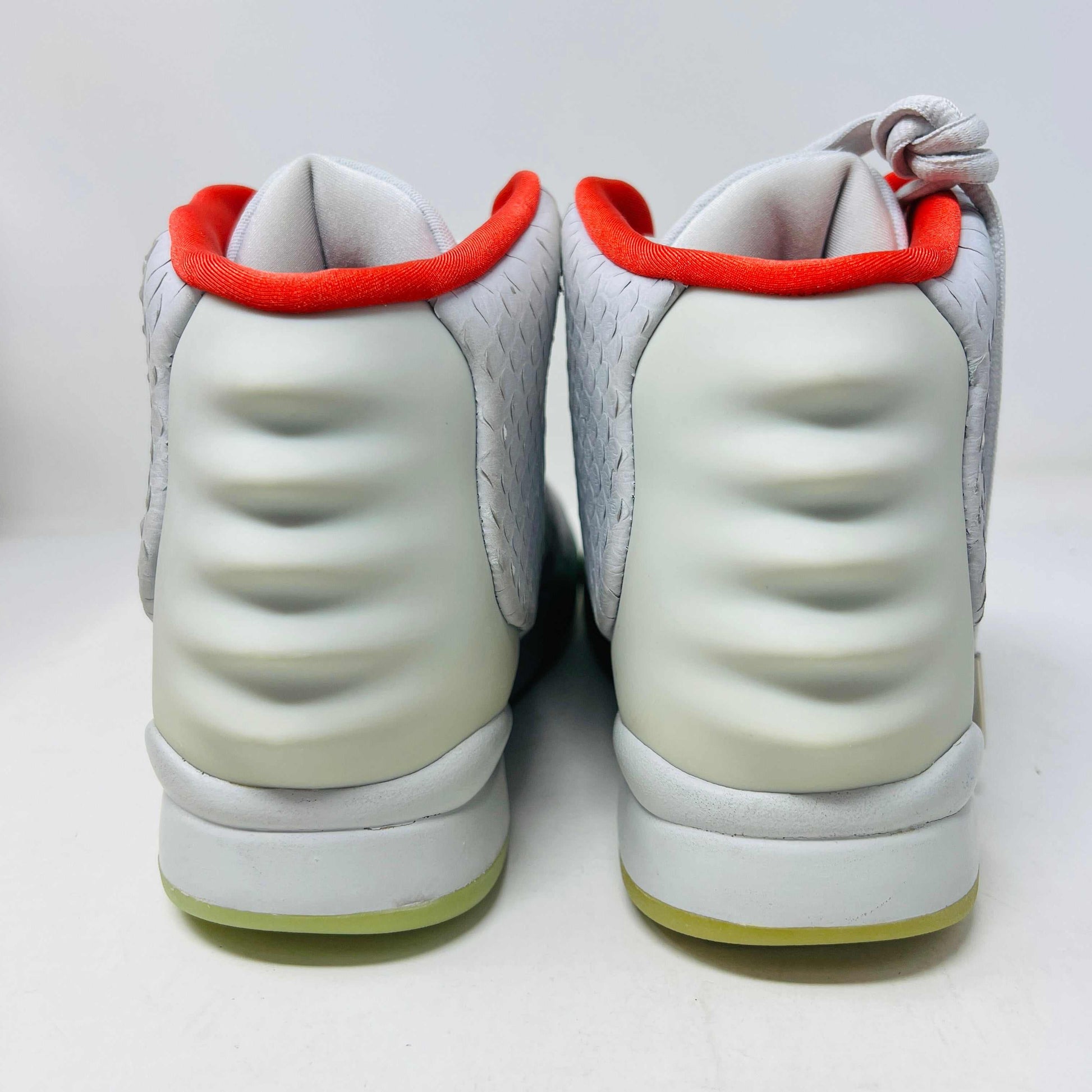 A pair of new Nike Air Yeezy 2 Pure Platinum high-tops rests on a cardboard box. The sneakers are mostly gray with a red lining, midfoot strap, and green-tinted soles. The label reads Air Yeezy 2 NRG, size 9, showcasing authentic detailing by Nike.
