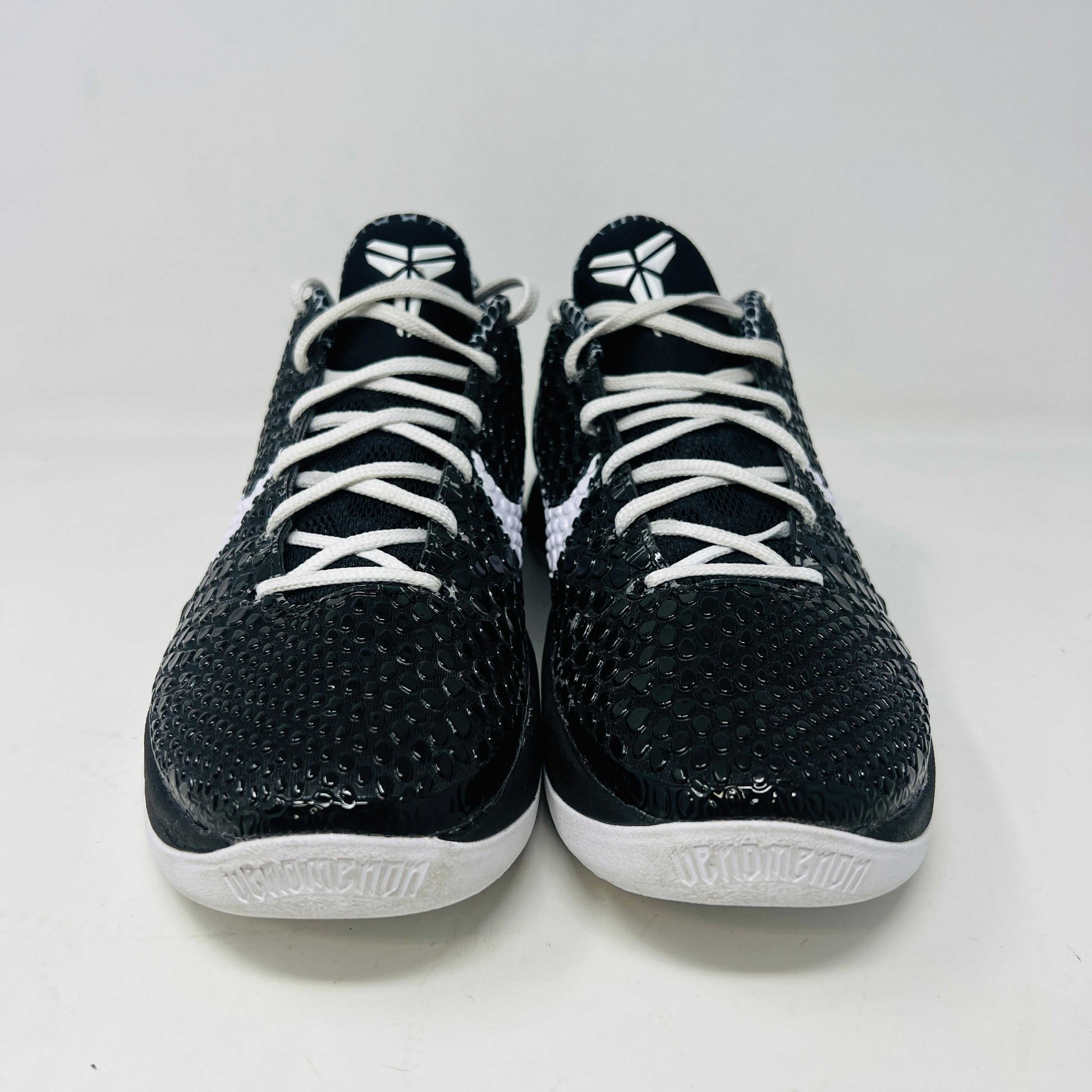 The black and white Nike Kobe 6 Protro Mambacita Sweet 16 shoe features a glossy finish, a gold number 2 on the heel, and light wear with a minor scratch on the back tab. It comes in sizes 8 and 9.5, displayed on a black box labeled Kobe V Proto, and is guaranteed authentic by KOBE.