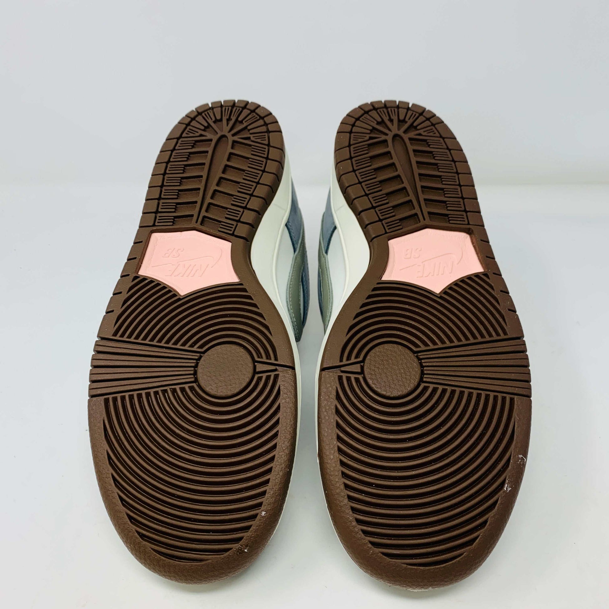 The Nike SB Dunk Low Yuto Horigome sneaker, with a white and light blue design featuring a gray swoosh, is displayed on a white Nike SB box. The authentic shoe has pink and brown laces, a brown sole, and an embroidered logo on the heel.