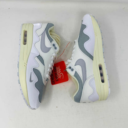 The Nike Air Max 1 Patta Waves White, a brand new sneaker, features a visible air cushion sole and swoosh logo. It comes elegantly displayed on a matching P.G.L.F.A. box with extra laces in a plastic bag attached to the tongue.