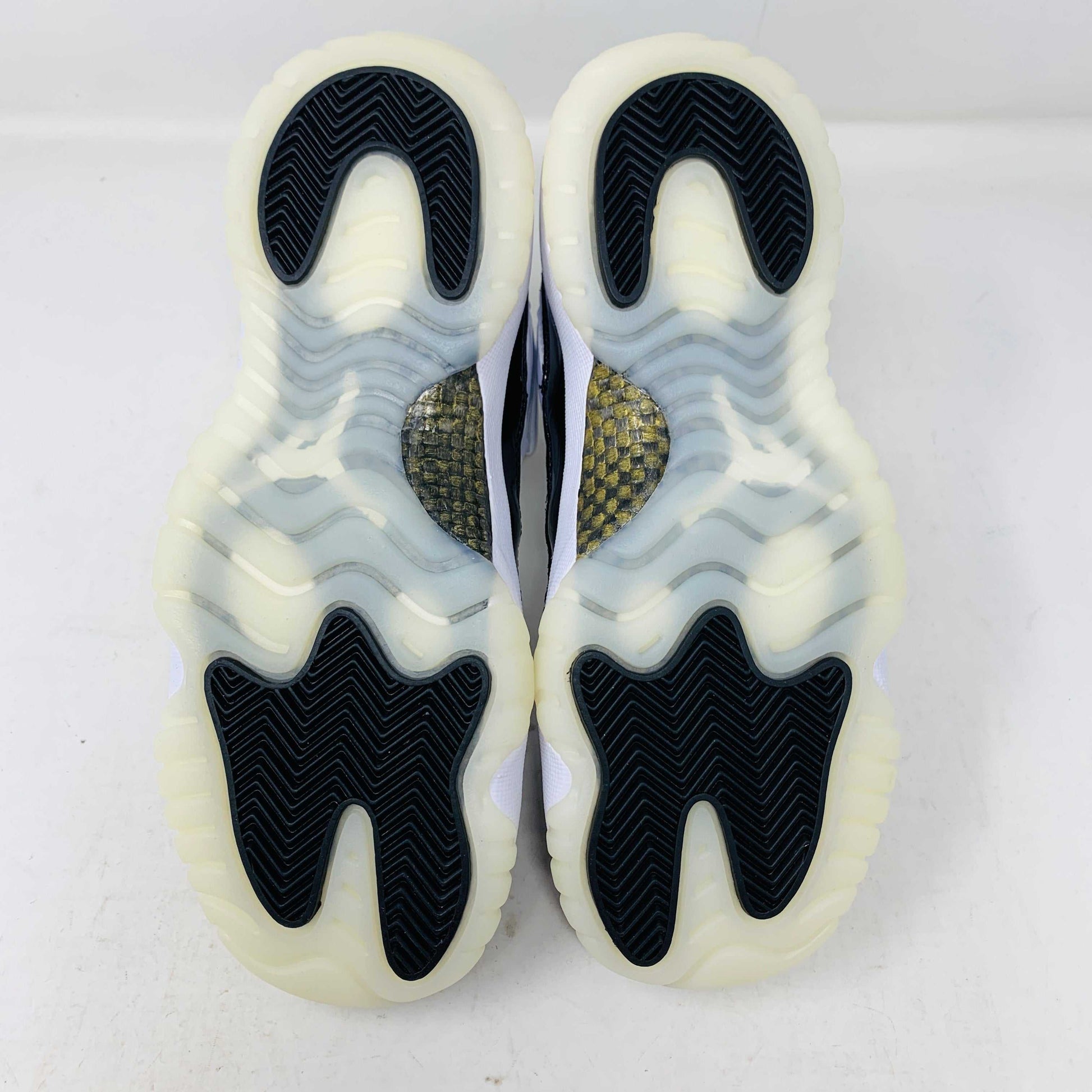 A pair of authentic Jordan 11 Retro DMP Gratitude (2023) (GS) sneakers, featuring a glossy white and black finish with a gold logo, is placed on top of a gray Nike Air shoebox.