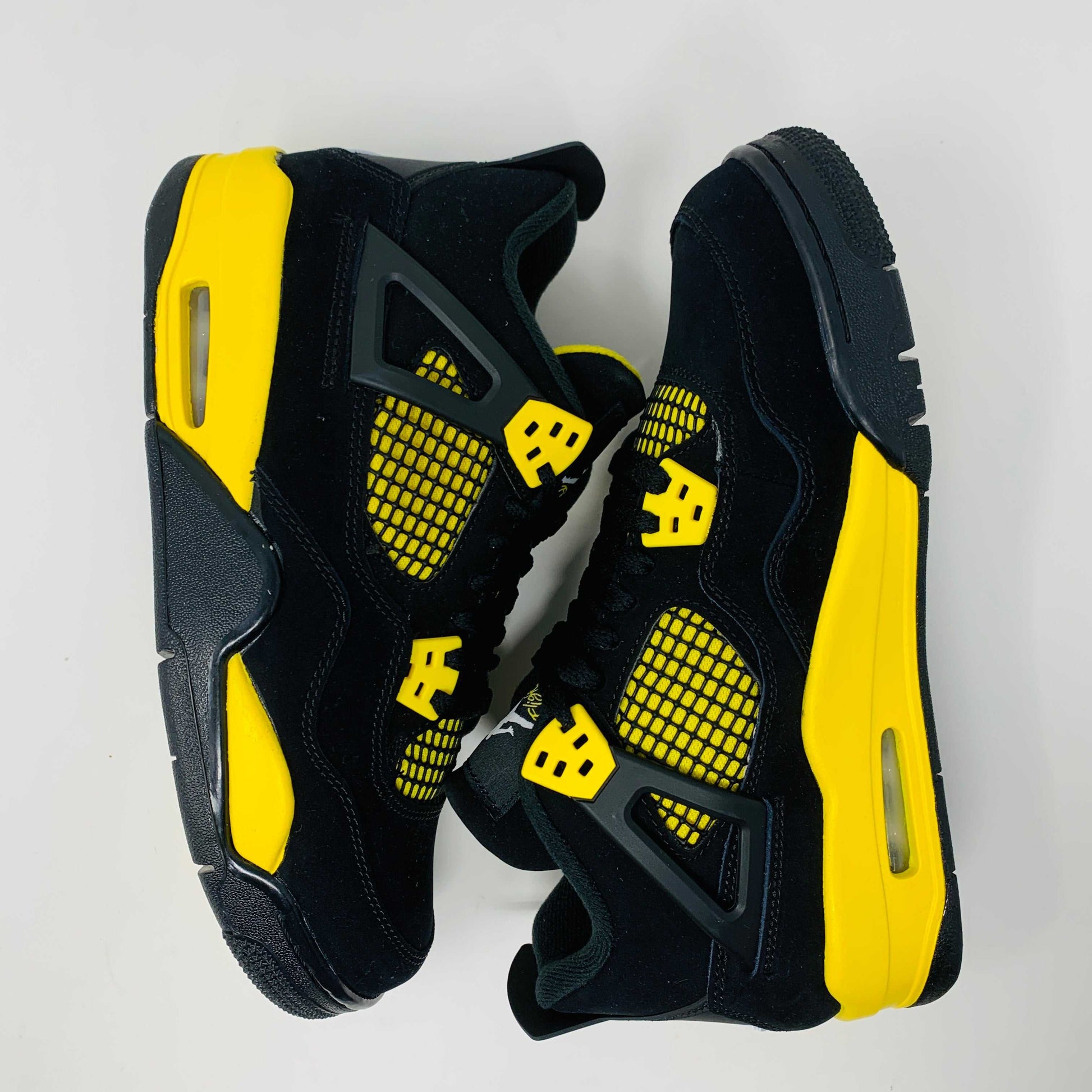 Brand new for 2023, the Jordan 4 Retro Thunder (GS) sneakers in black and yellow feature mesh panels and air cushioning. Positioned on a white background, they showcase their unique color scheme and design.