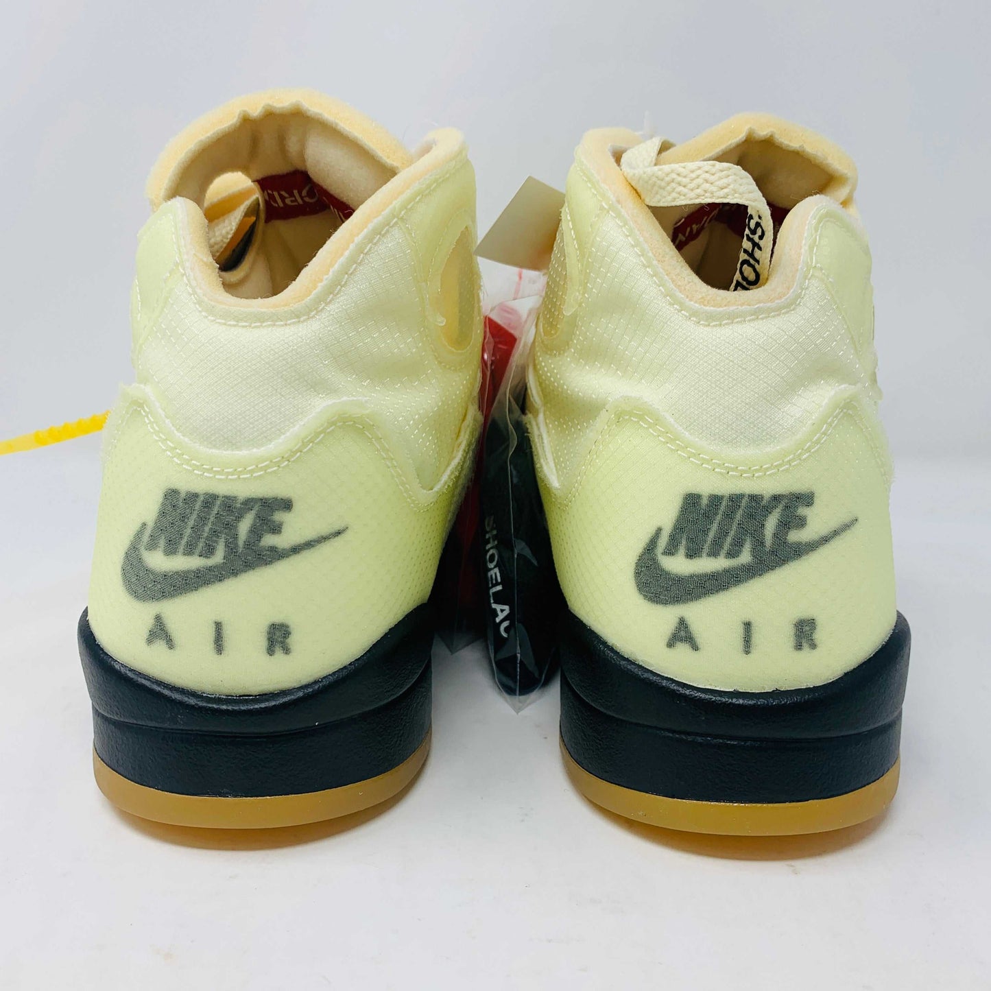 The Jordan 5 Off White Sail sneakers feature a yellow and black design with red accents, a visible air unit, and the number 23 on the side. BRAND NEW in a black shoebox with a red Jumpman logo and speckled base, they include an attached yellow tag and come with EXTRA LACES for versatility.