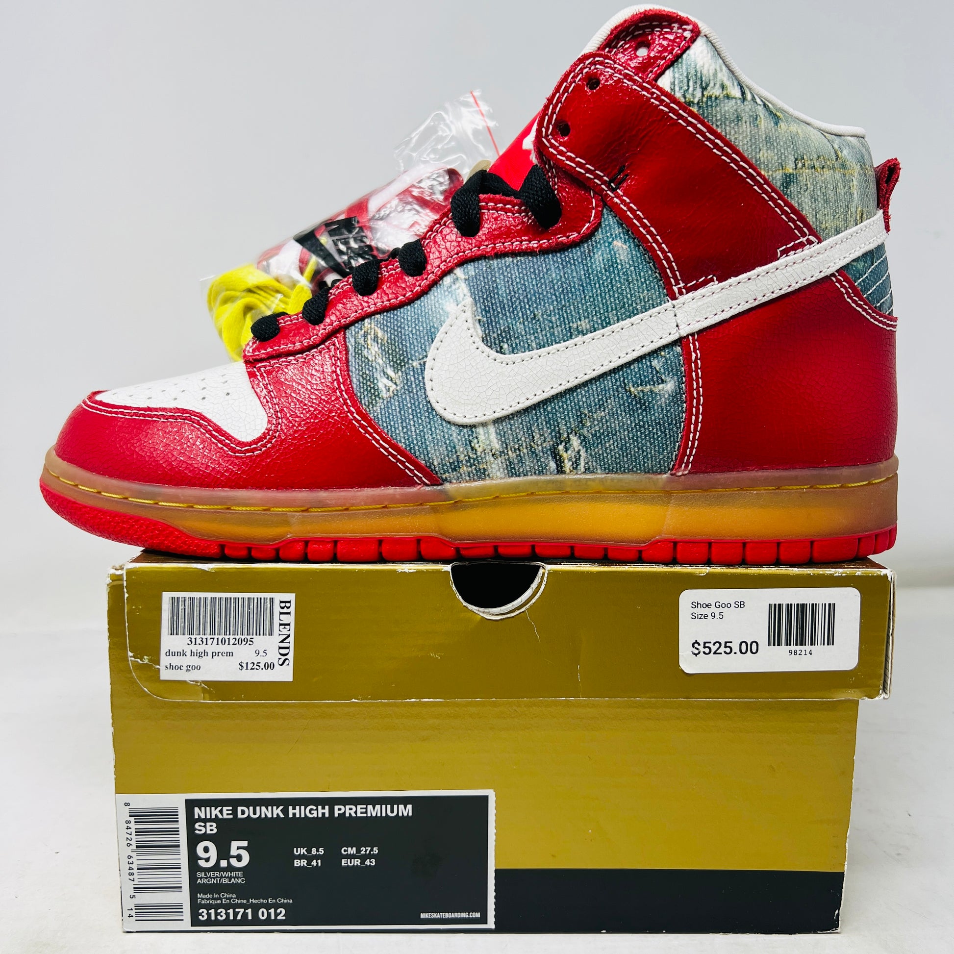 The Nike SB Dunk High Shoe Goo from 2008, priced at $525, sits atop its box. It features red and blue denim sections, a white swoosh, and a gum sole. A tag shows size and numbers, with extra laces beside the shoebox.