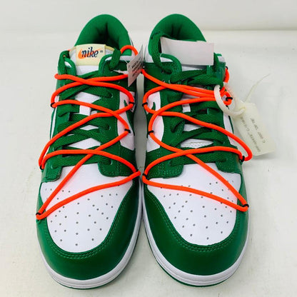 The Nike Dunk Low Off White Pine Green sneaker, accented with bright orange laces, rests on a shiny silver box. This authentic 2019 release by Nike boasts a sleek white tag, highlighting its new allure.
