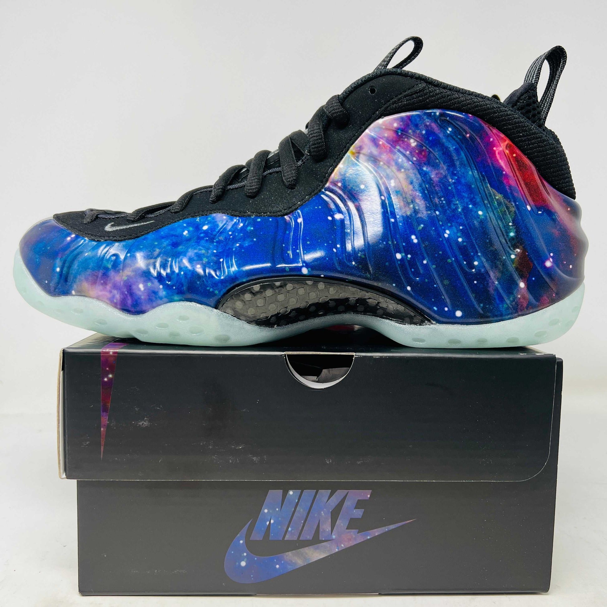 The 2025 Nike Air Foamposite One Galaxy sneaker features a vibrant galaxy design on the upper, complemented by a dark sole and black laces. Presented atop its black box, this edition is an essential piece for collectors.