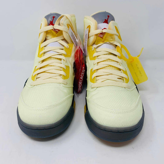 The Jordan 5 Off White Sail sneakers feature a yellow and black design with red accents, a visible air unit, and the number 23 on the side. BRAND NEW in a black shoebox with a red Jumpman logo and speckled base, they include an attached yellow tag and come with EXTRA LACES for versatility.
