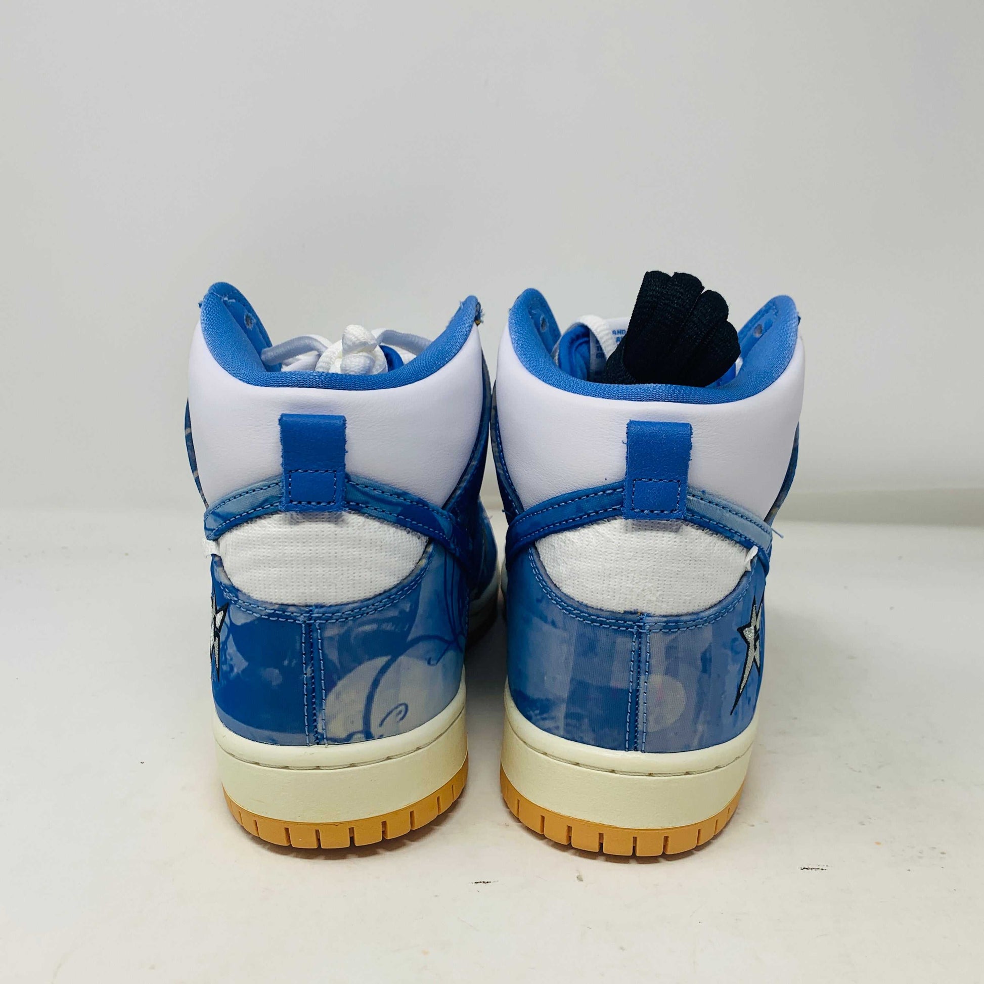 The Nike SB Dunk High Carpet Company sneakers feature a blue and white starry design, presented on a green and yellow Nike shoe box. Three extra laces in blue, yellow, and white are included to ensure your style is 100% authentic.