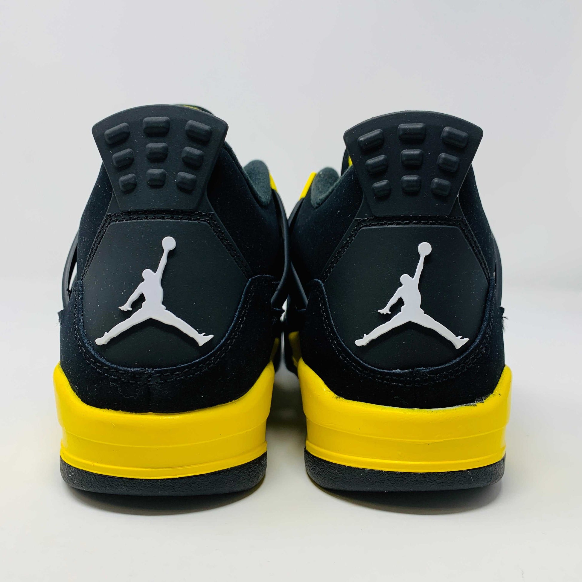 Brand new for 2023, the Jordan 4 Retro Thunder (GS) sneakers in black and yellow feature mesh panels and air cushioning. Positioned on a white background, they showcase their unique color scheme and design.