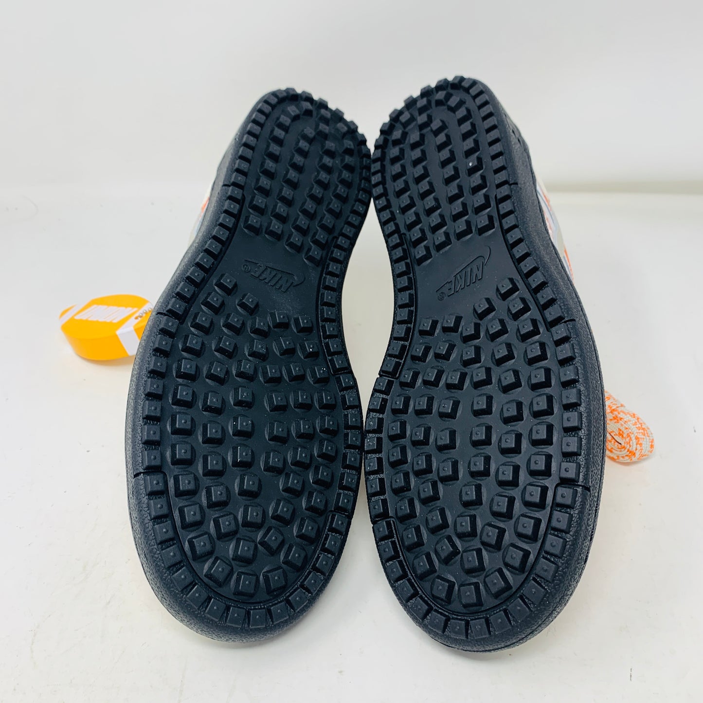 The pristine Nike Field General Union LA Ivory sneakers, in white and orange with black soles, rest on an orange box. Featuring a UNION tag, Nike logo, and a blue sticker with a silhouetted man, theyre perfect for any accessories collection.