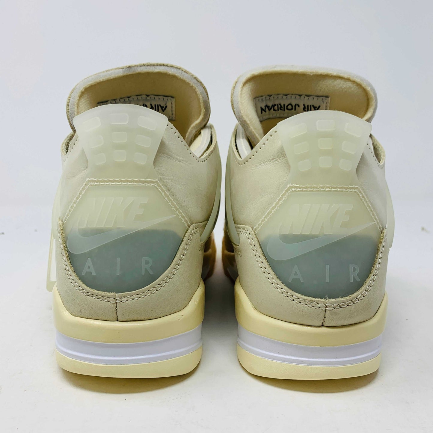 A beige Jordan 4 Off White Sail W sneaker rests on a box with the authentic Air Jordan logo. It comes with three extra sets of laces in mint, cream, and black labeled SHOELACES, a plastic zip tie, and features a small Jumpman Air tag.