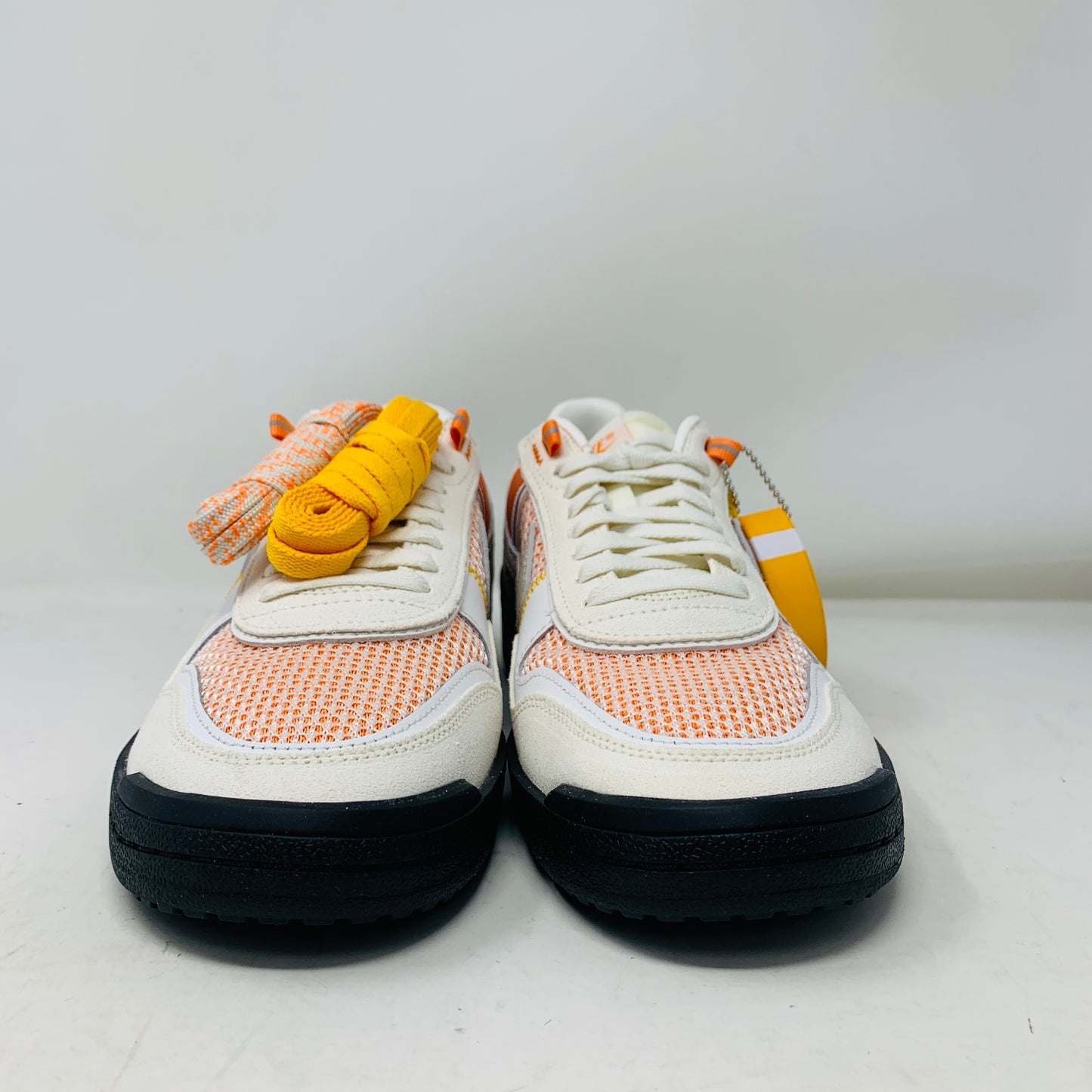 The pristine Nike Field General Union LA Ivory sneakers, in white and orange with black soles, rest on an orange box. Featuring a UNION tag, Nike logo, and a blue sticker with a silhouetted man, theyre perfect for any accessories collection.