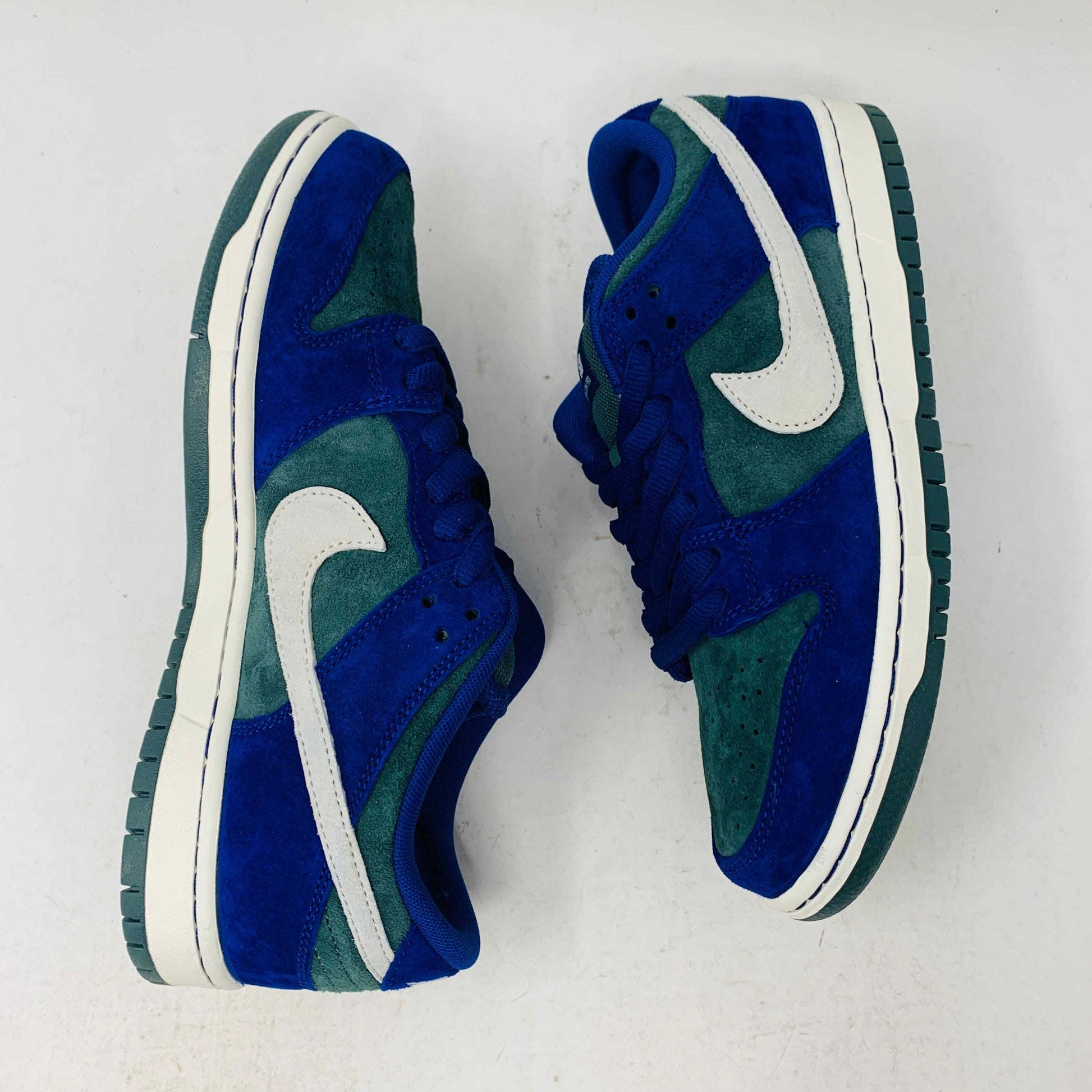 The Nike SB Dunk Low Deep Royal Blue sneaker, featuring a sleek blue and green design with a white swoosh, sits atop a purple Nike box. A bonus set of green laces accompanies the shoe, perfect for updating your style in 2024.
