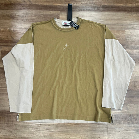 A brand new Supreme Stone Island L/S Top in tan, size large, is laid flat on a wooden floor. It features beige sleeves, a small logo on the chest, and a black tag attached to the collar.