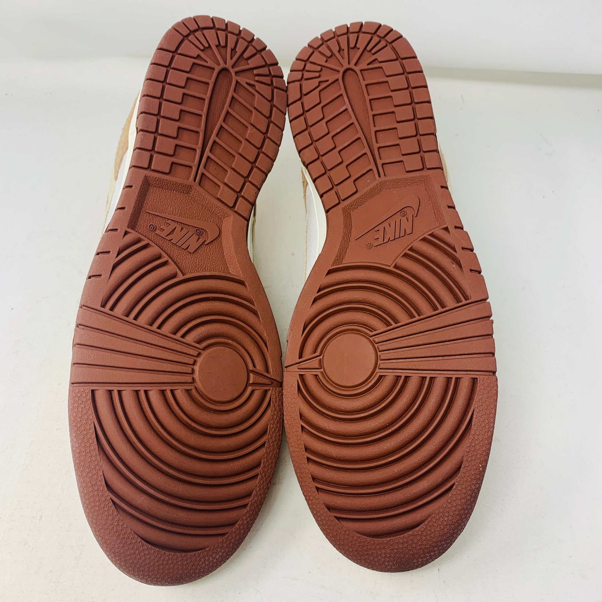 A brand new pair of Nike Dunk Low Medium Curry sneakers, with a beige suede upper and white swoosh accents, rests in pristine condition on a red box featuring the bold white Nike logo, set against a plain backdrop.