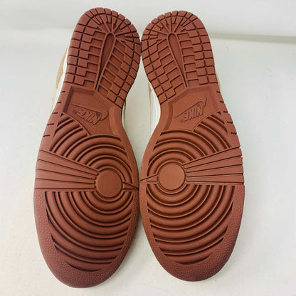 A brand new pair of Nike Dunk Low Medium Curry sneakers, with a beige suede upper and white swoosh accents, rests in pristine condition on a red box featuring the bold white Nike logo, set against a plain backdrop.