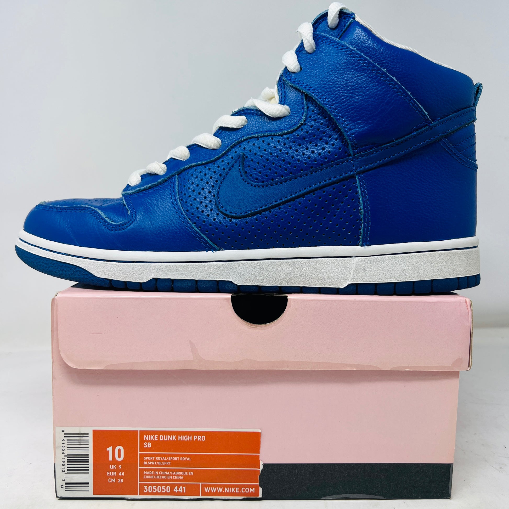 A Nike SB Dunk High T19 Royal Blue sneaker with white laces is perched on a pristine pink shoebox, showcasing the iconic Nike swoosh. The box, in excellent condition, displays a size 10 label.