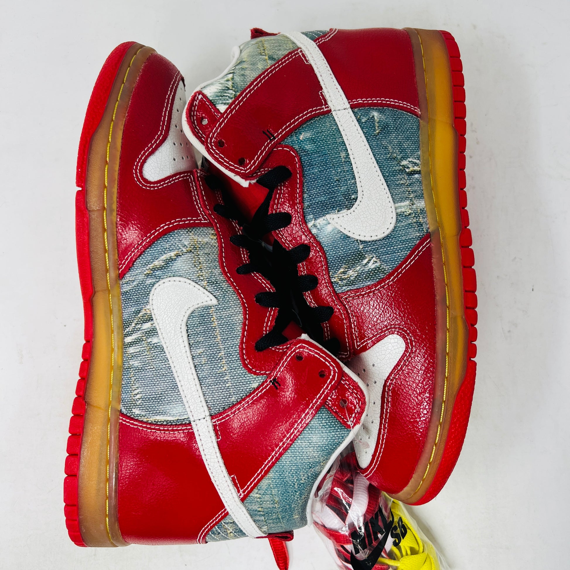The Nike SB Dunk High Shoe Goo from 2008, priced at $525, sits atop its box. It features red and blue denim sections, a white swoosh, and a gum sole. A tag shows size and numbers, with extra laces beside the shoebox.