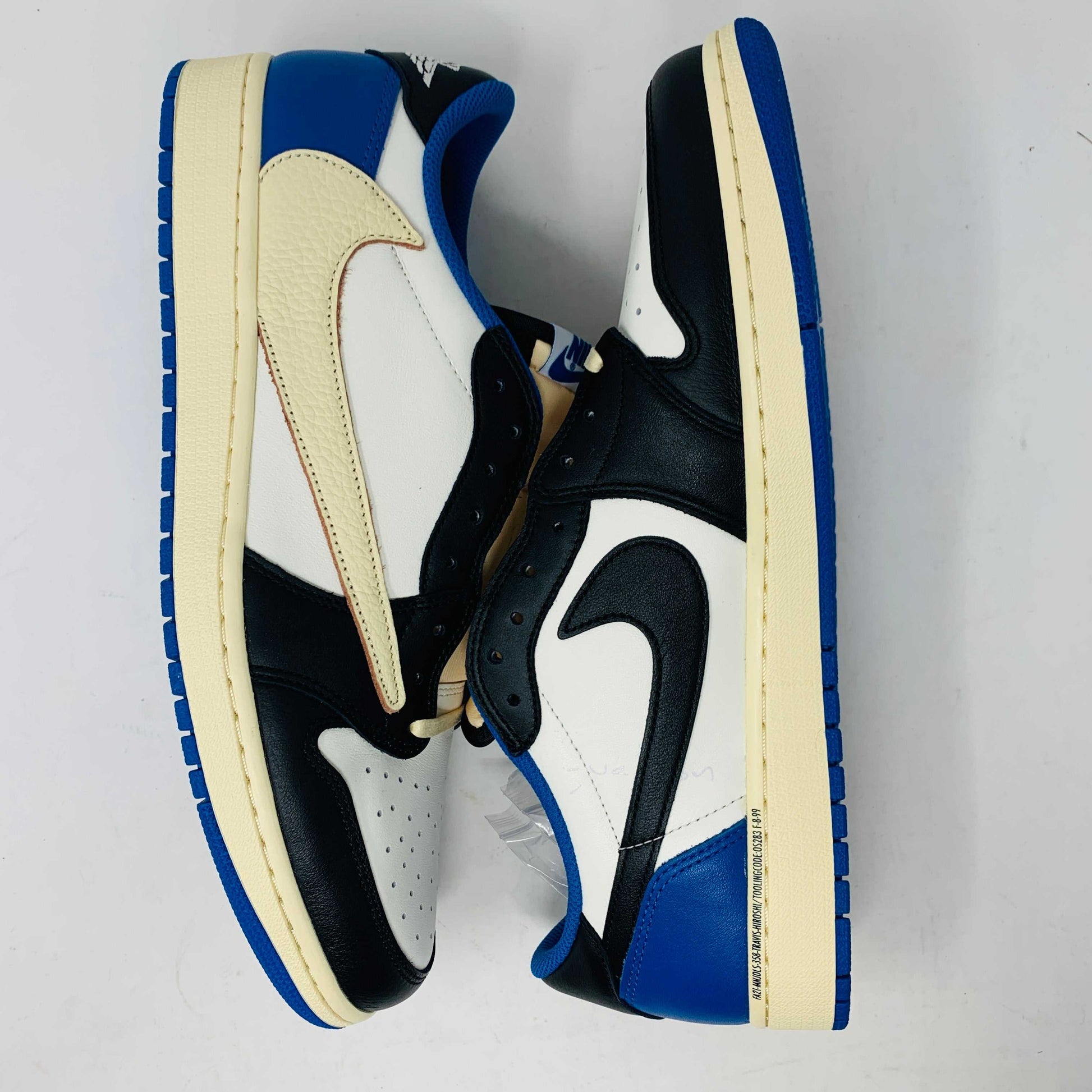 The Jordan 1 Low Travis Scott x Fragment sneakers feature a black and white leather upper with blue accents, a unique beige backward swoosh, and come in a branded Nike box with graphics. These brand-new shoes include an extra set of laces for added versatility.
