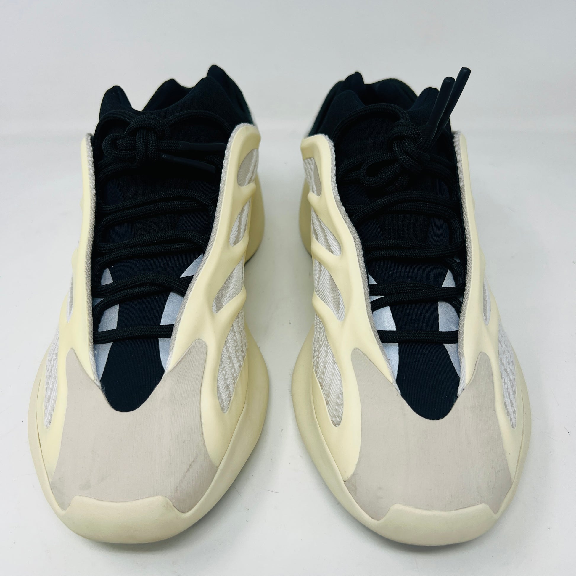 The adidas Yeezy 700 V3 Azael features a futuristic design with a black mesh upper, white and beige sculpted overlays, and an intricate lacing system. It has a sleek, modern look set against a plain white background, showing minimal wear for that fresh out-of-the-box condition.