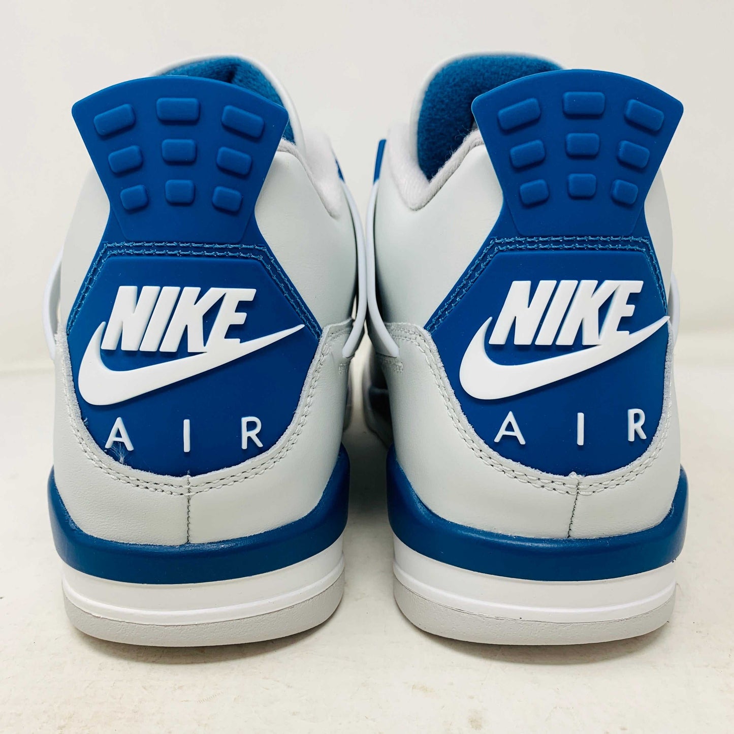 The Jordan 4 Retro Military Blue (2024) sneaker, with white and blue mesh details and a visible air cushion, rests on a black speckled NIKE AIR box with bold orange text. It is 100% authentic, including orange tags, ensuring it’s brand new.