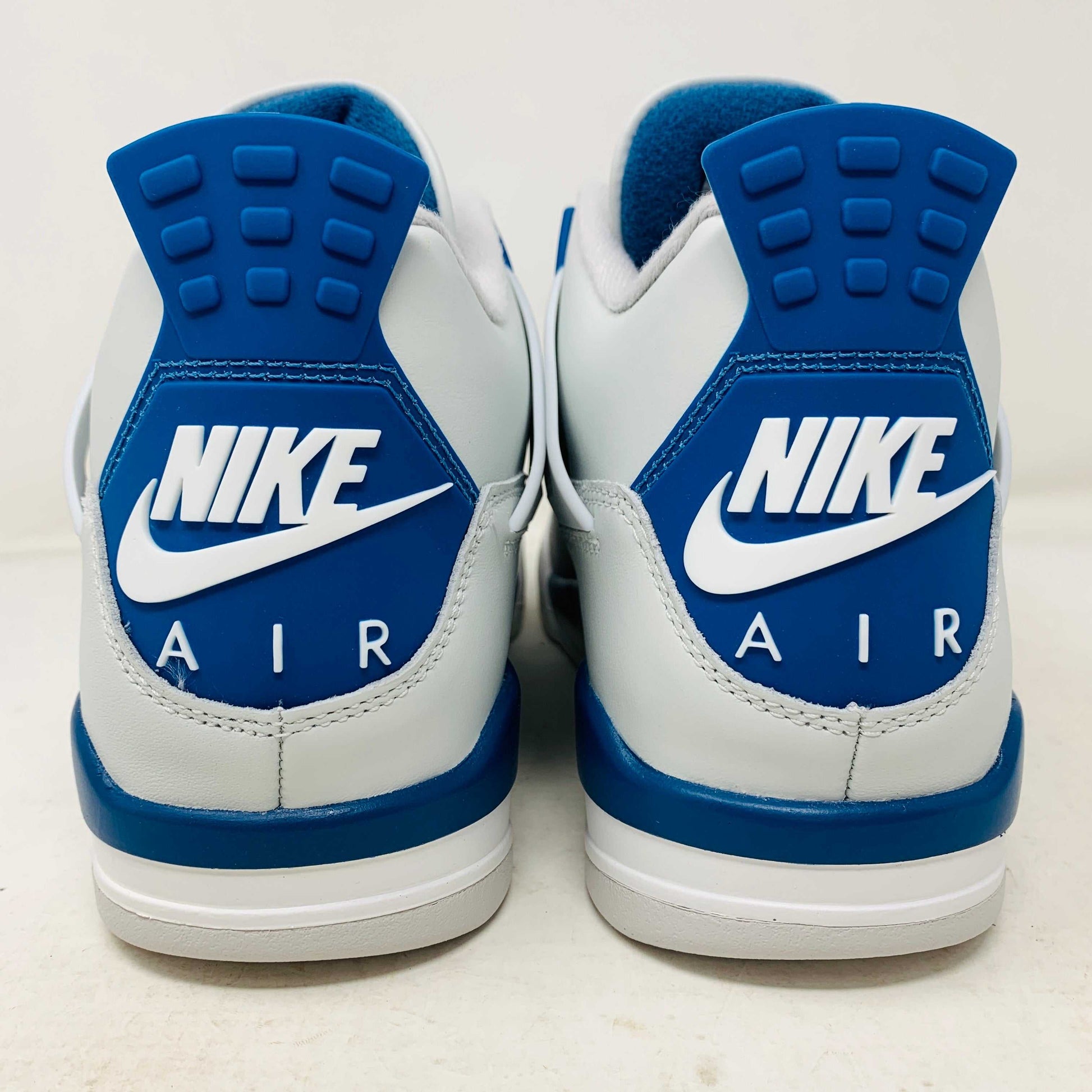The Jordan 4 Retro Military Blue (2024) sneaker, with white and blue mesh details and a visible air cushion, rests on a black speckled NIKE AIR box with bold orange text. It is 100% authentic, including orange tags, ensuring it’s brand new.