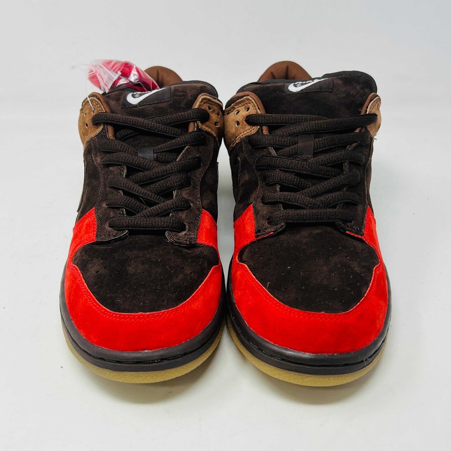 A pair of BRAND NEW Nike SB Dunk Low Bison sneakers featuring brown and red suede uppers, black laces, EXTRA LACES included, and a light brown sole. Positioned side by side on a white background, they promise to be 100% authentic and stylish.
