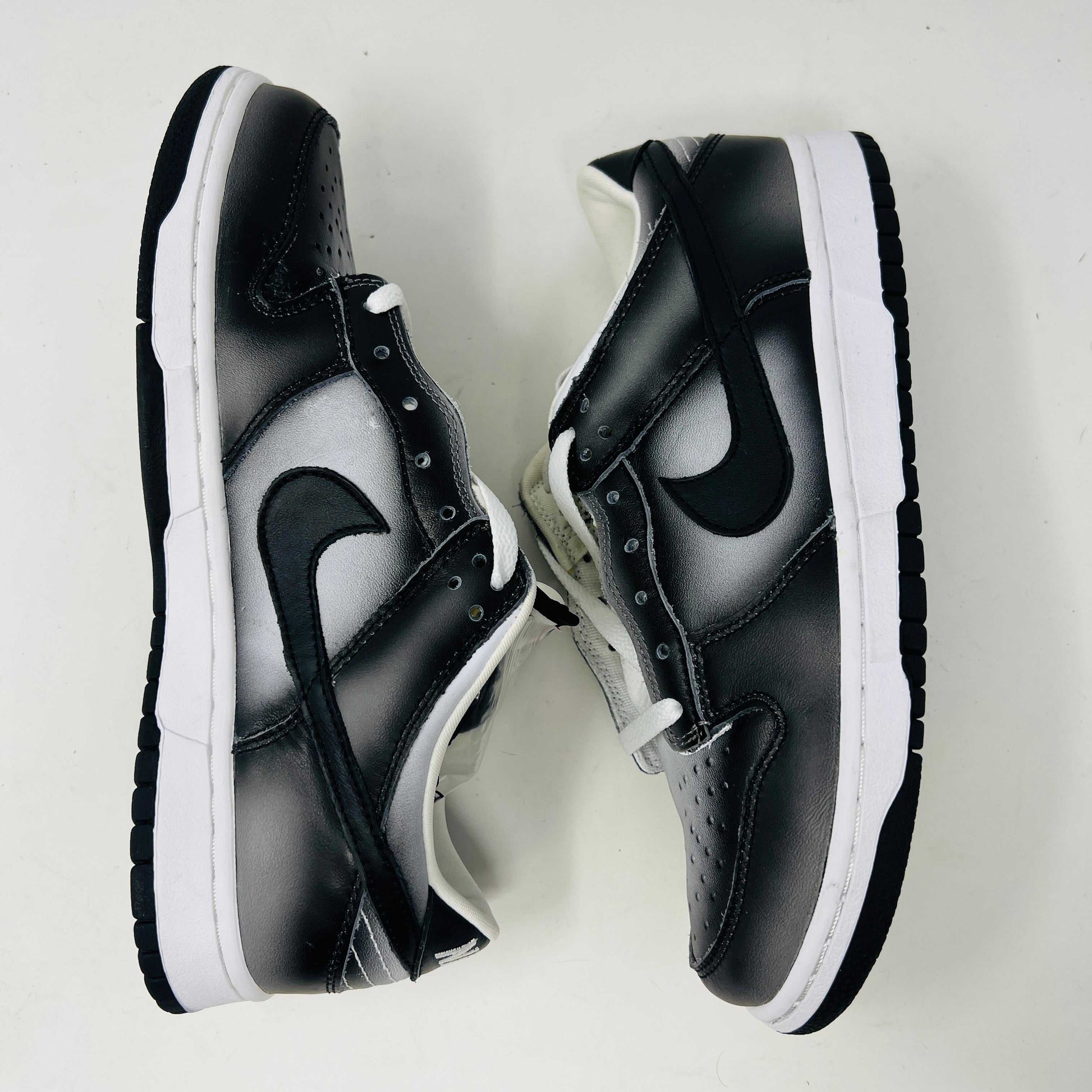 Authentic Nike Dunk Low Haze sneakers in black and white with white laces are displayed front-on against a white backdrop. A clear bag with extra black laces is on the left shoe.