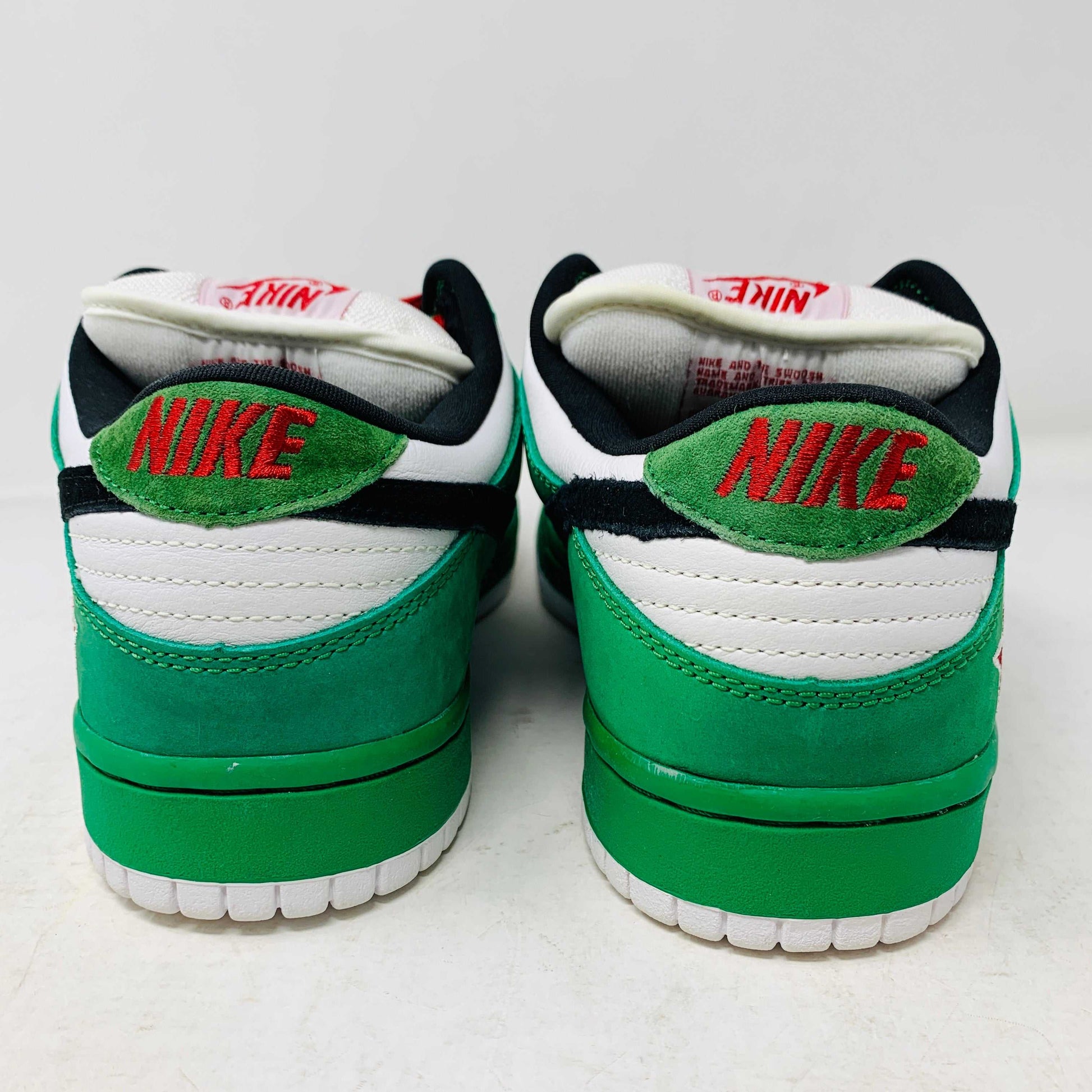 The Nike SB Dunk Low Heineken sneakers, with a green, white, and black color scheme and red branding on the heel, boast a low-top design viewed from the back.