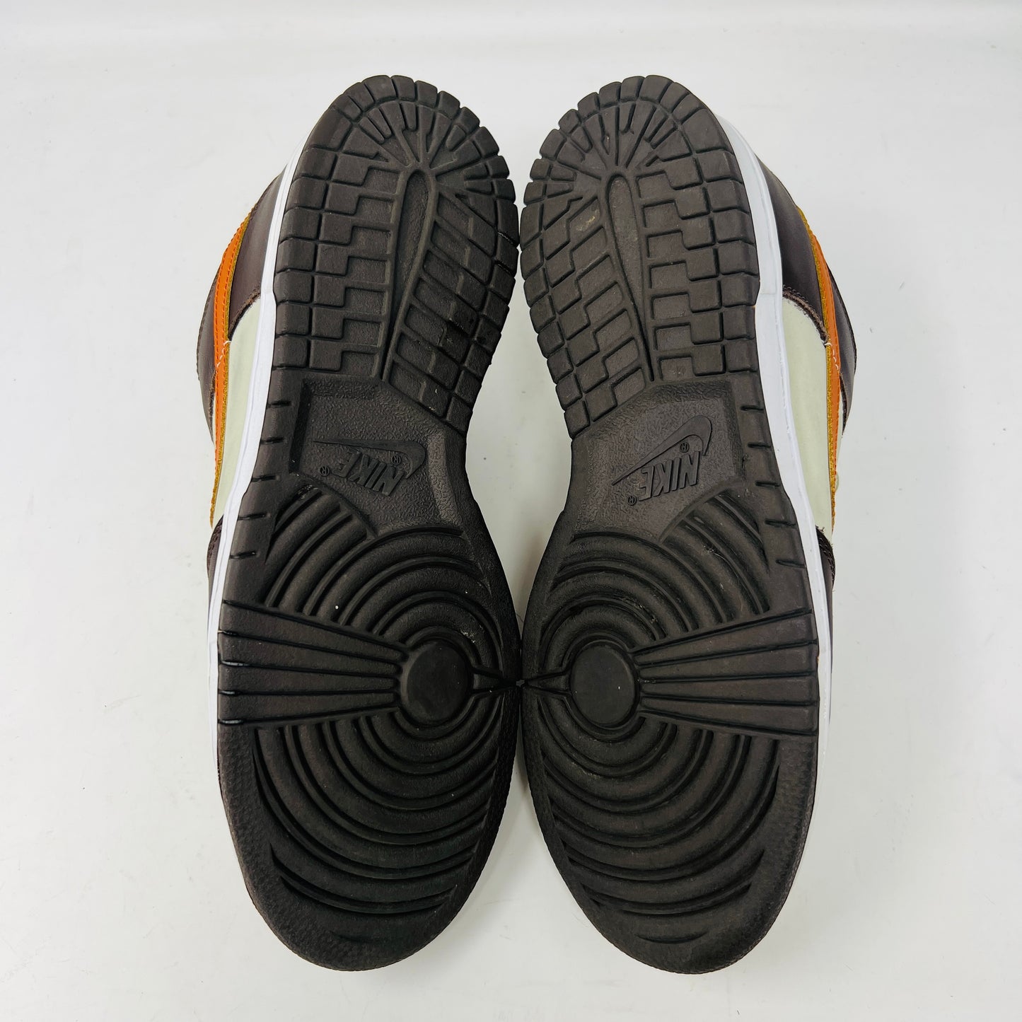 The Nike Dunk Low Pro B Light Stone Mesa Orange sneaker from 2002 is shown side-on, featuring sleek uppers in dark brown and cream with an orange swoosh. It rests elegantly on a white midsole with a black outsole against a plain background.