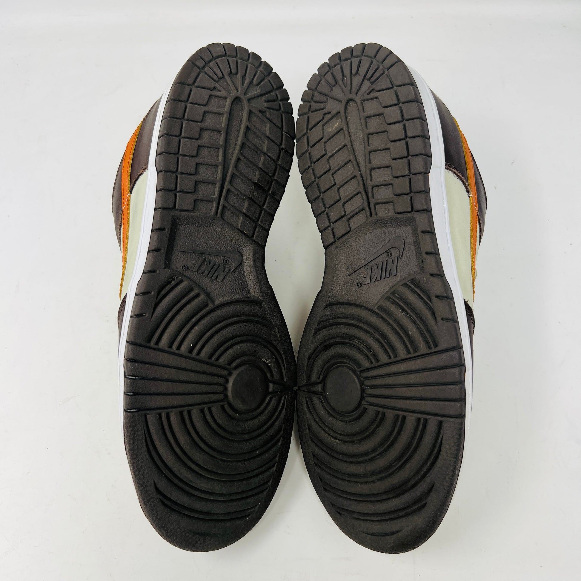 The Nike Dunk Low Pro B Light Stone Mesa Orange sneaker from 2002 is shown side-on, featuring sleek uppers in dark brown and cream with an orange swoosh. It rests elegantly on a white midsole with a black outsole against a plain background.